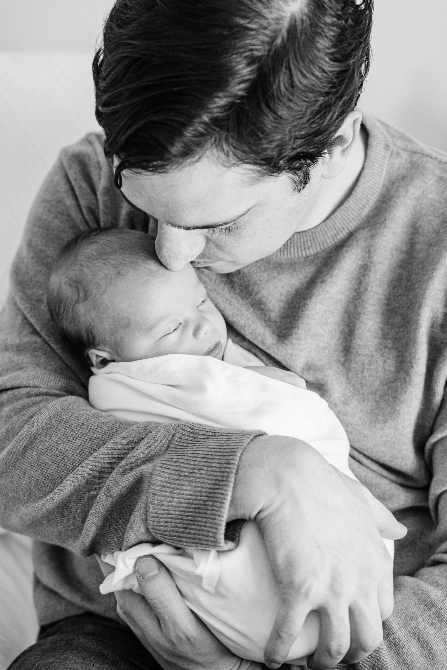 Black and white close-up photo of a baby being cradled and kissed in a tender moment.