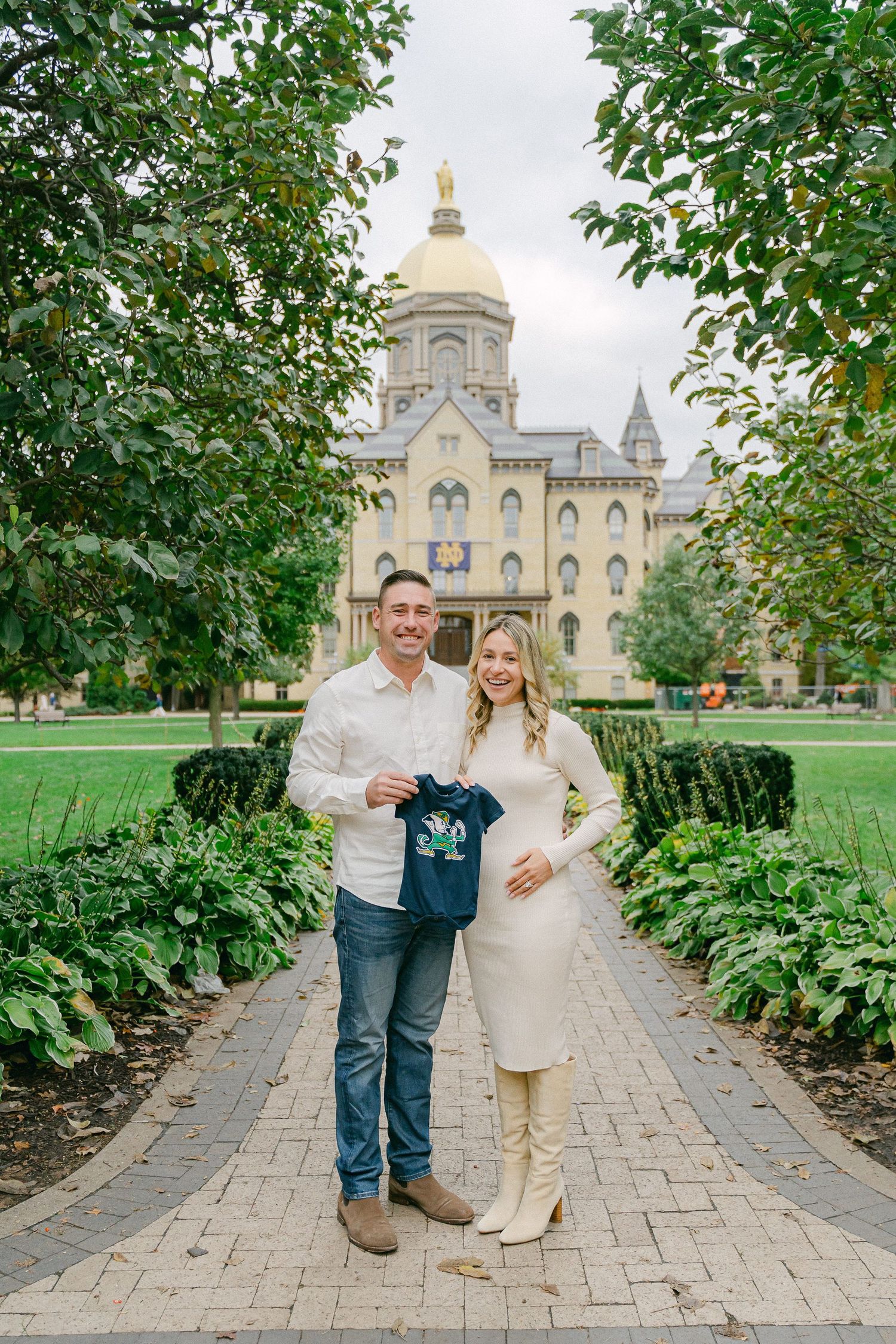 A couple shares a romantic moment on a stone path with a grand cathedral-style building visible in the background.
