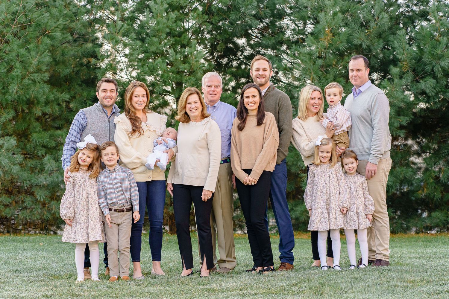 A group poses together outdoors in coordinated neutral-toned outfits against a lush green garden backdrop.