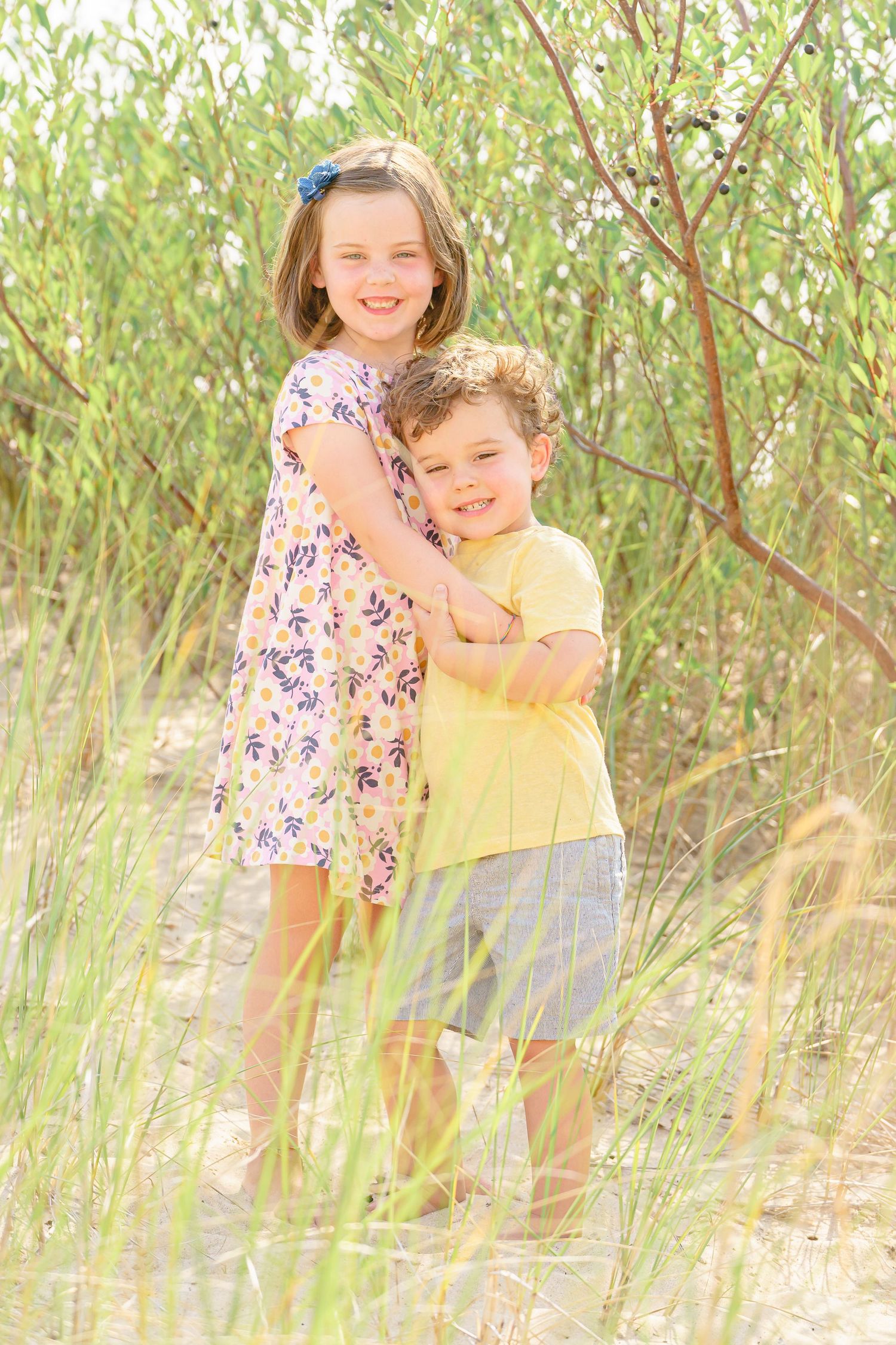 Two people share a joyful embrace while standing in tall grass on a bright sunny day.