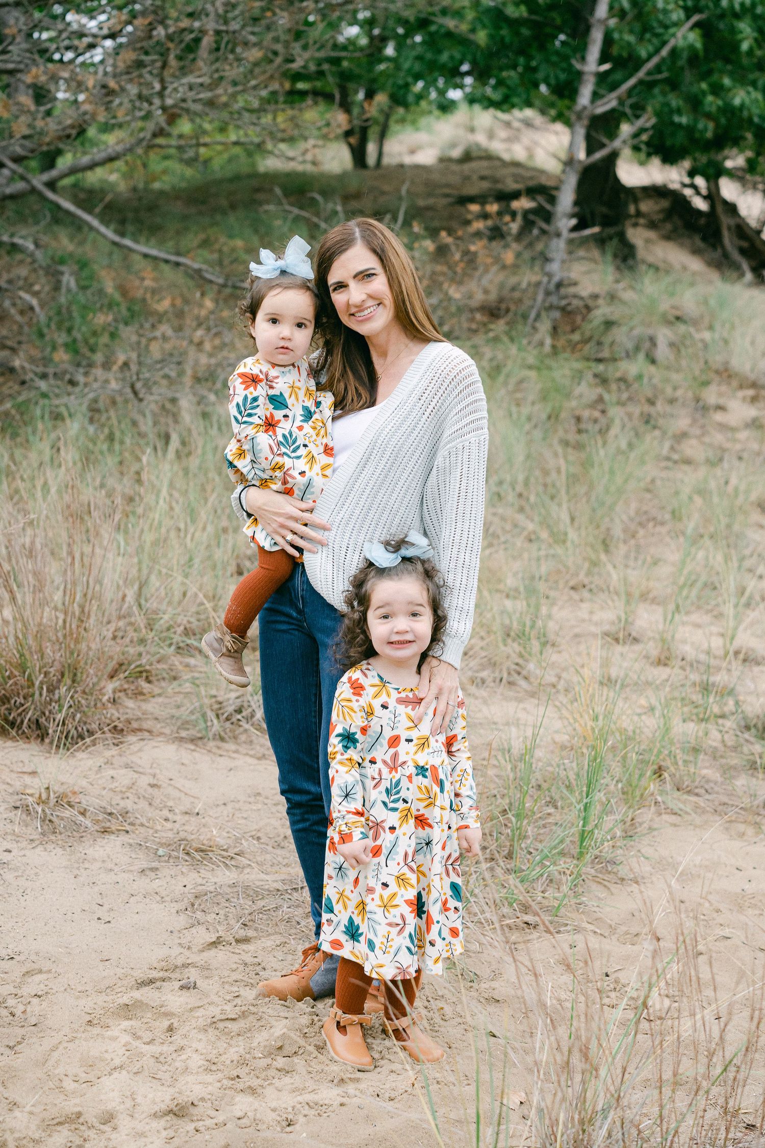 A family in coordinating outfits poses together in a natural outdoor setting with tall grass and trees.