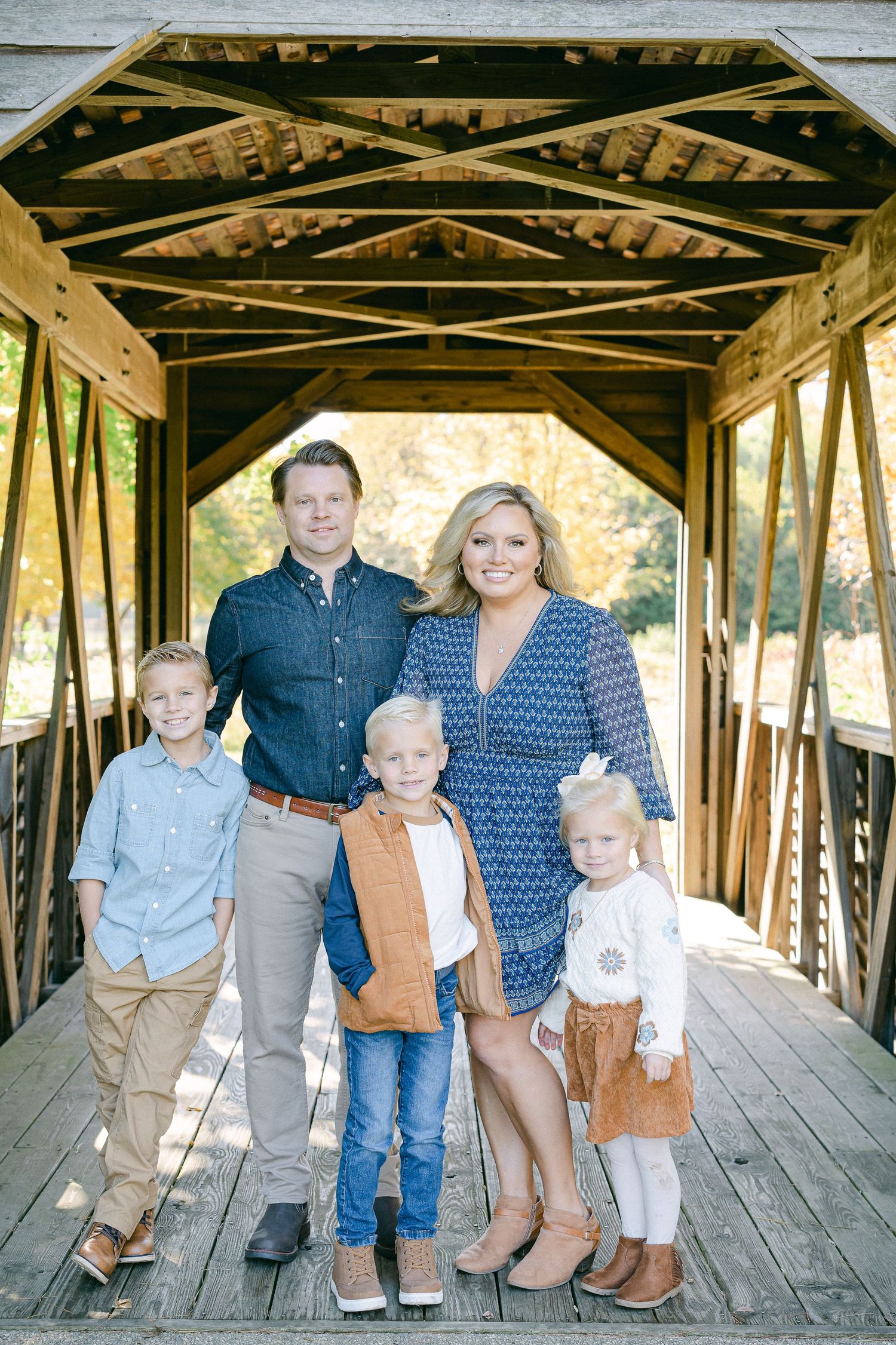 A family portrait taken inside a rustic wooden covered bridge with natural lighting.