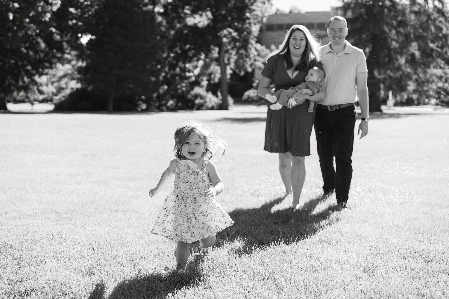 Black and white photo of a family walking together in a grassy field on a sunny day.