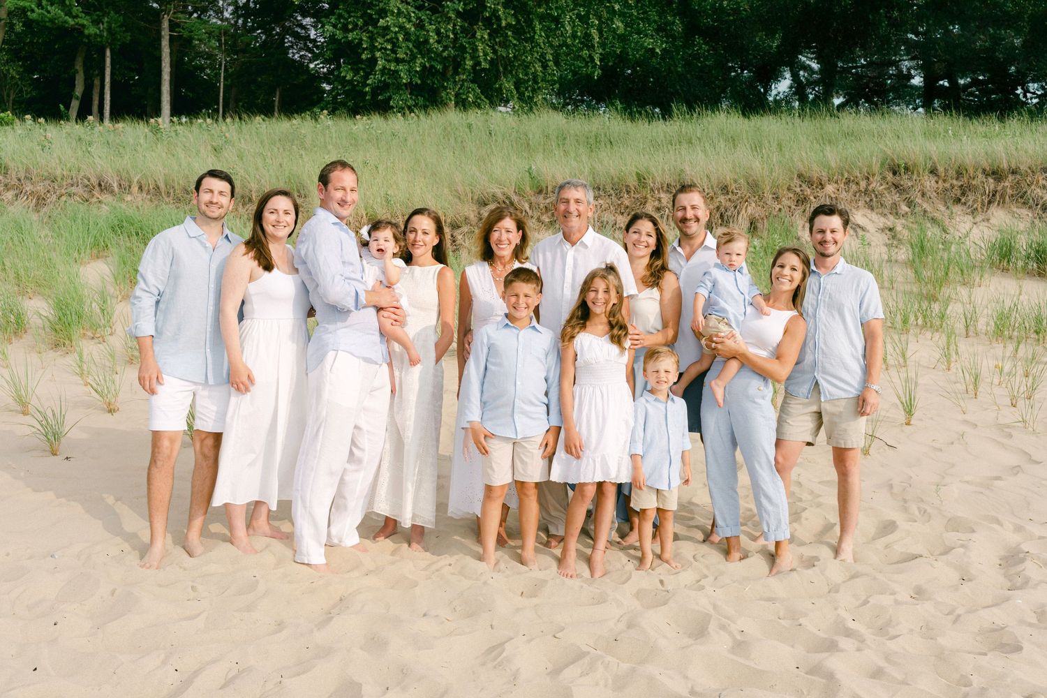 Group wearing coordinated white and blue outfits poses together on a sandy beach during summer.