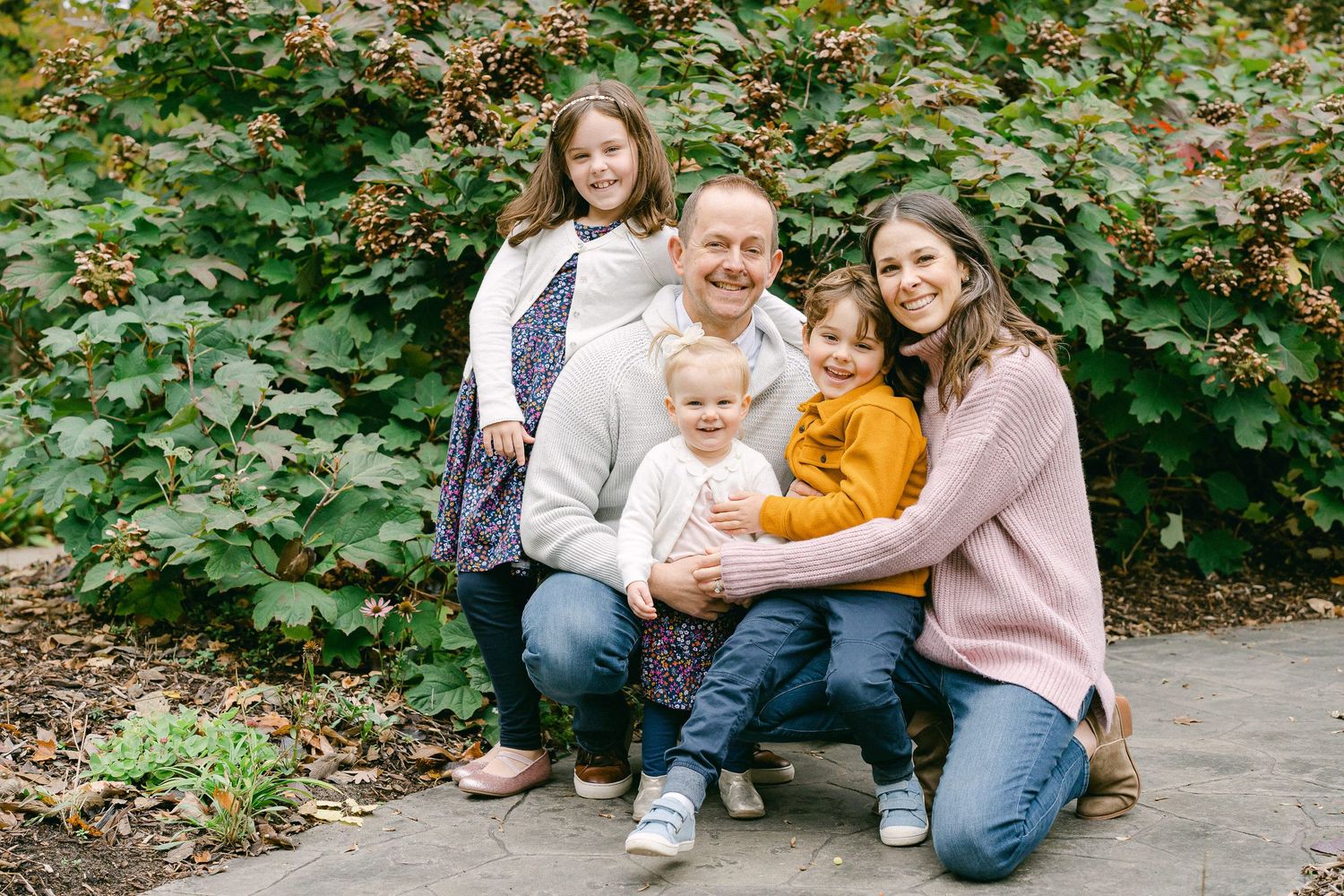 A family sits together outdoors in casual clothing for a series of candid photo portraits in a natural setting.