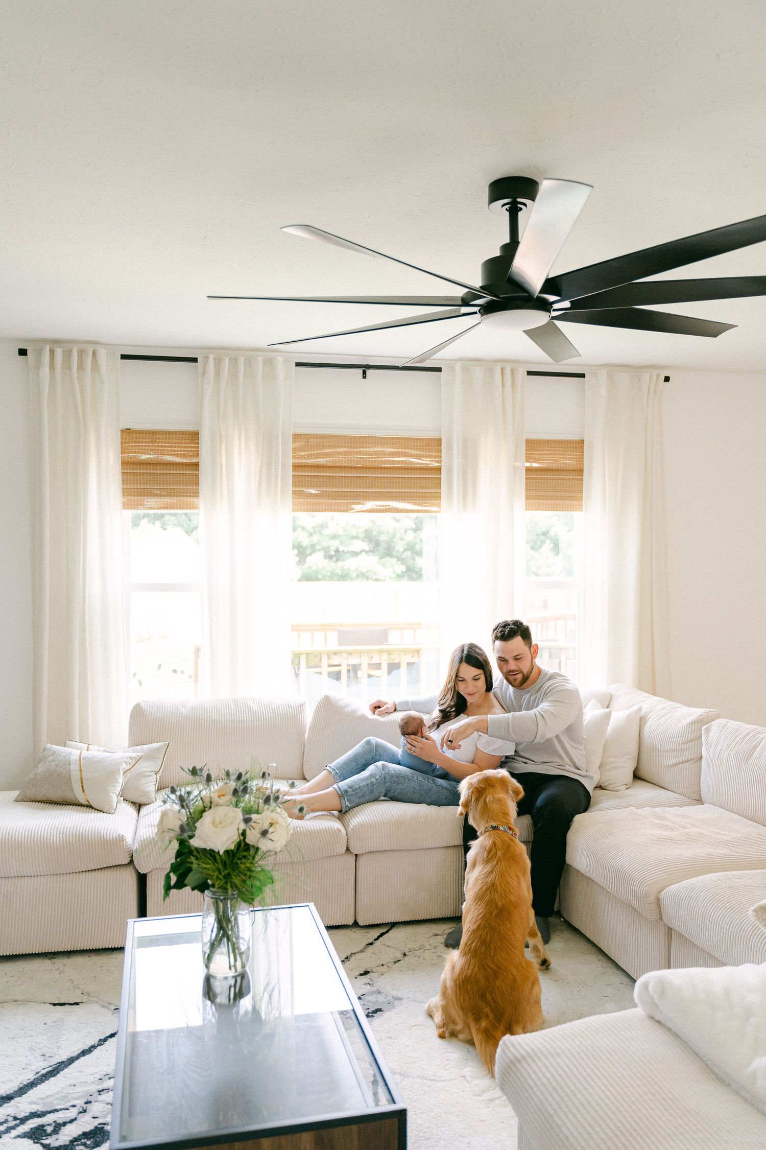 A bright white living room with coastal decor features people relaxing on sofas while a golden retriever looks on.