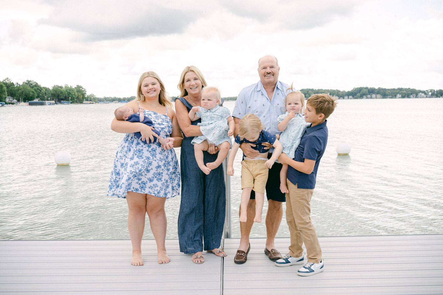 Family enjoying a summer day together on a white wooden dock by the lake wearing coordinating blue and white outfits.