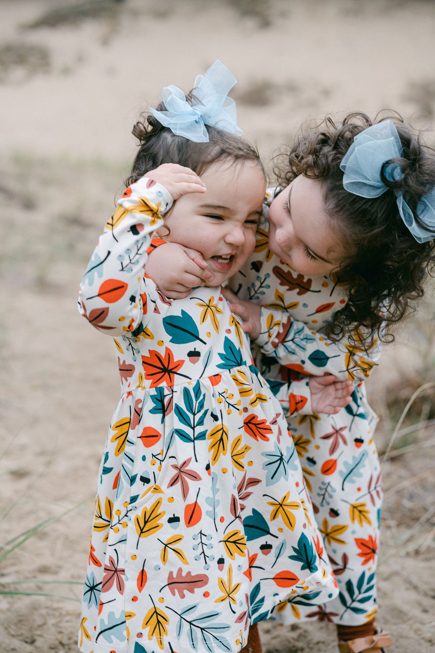 Two children in matching floral dresses share a sweet moment together outdoors.