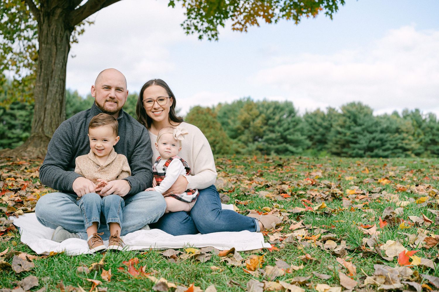 A family enjoys quality time together laying on fallen autumn leaves in a park setting.