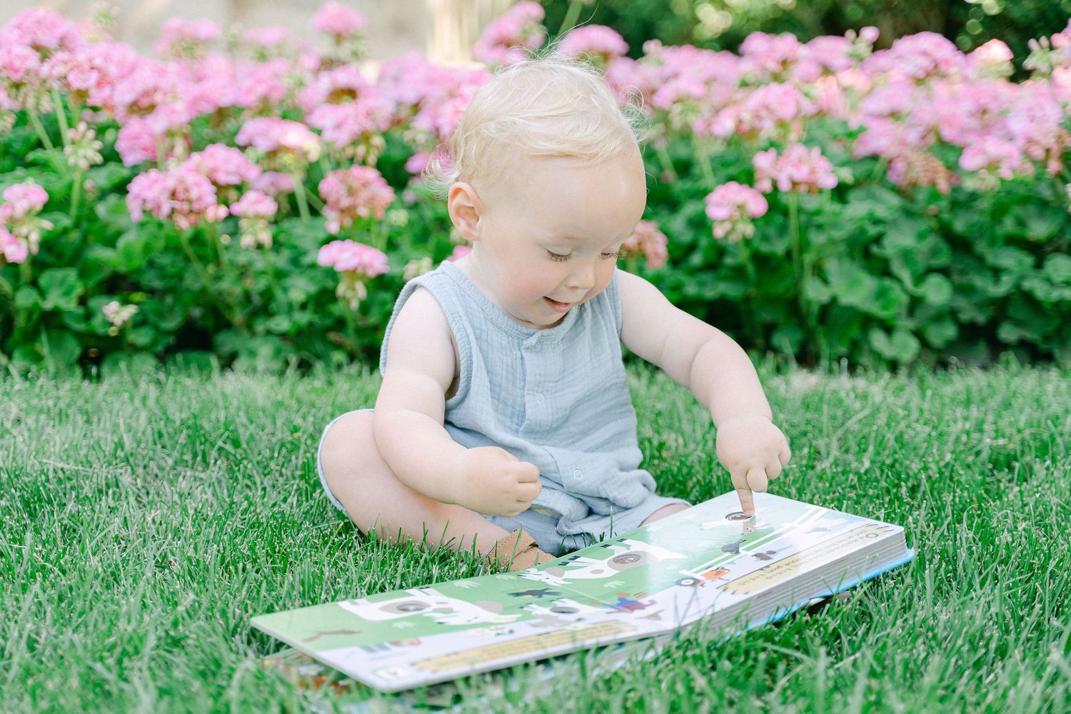 Child reading a picture book while lying on lush green grass in a garden setting.