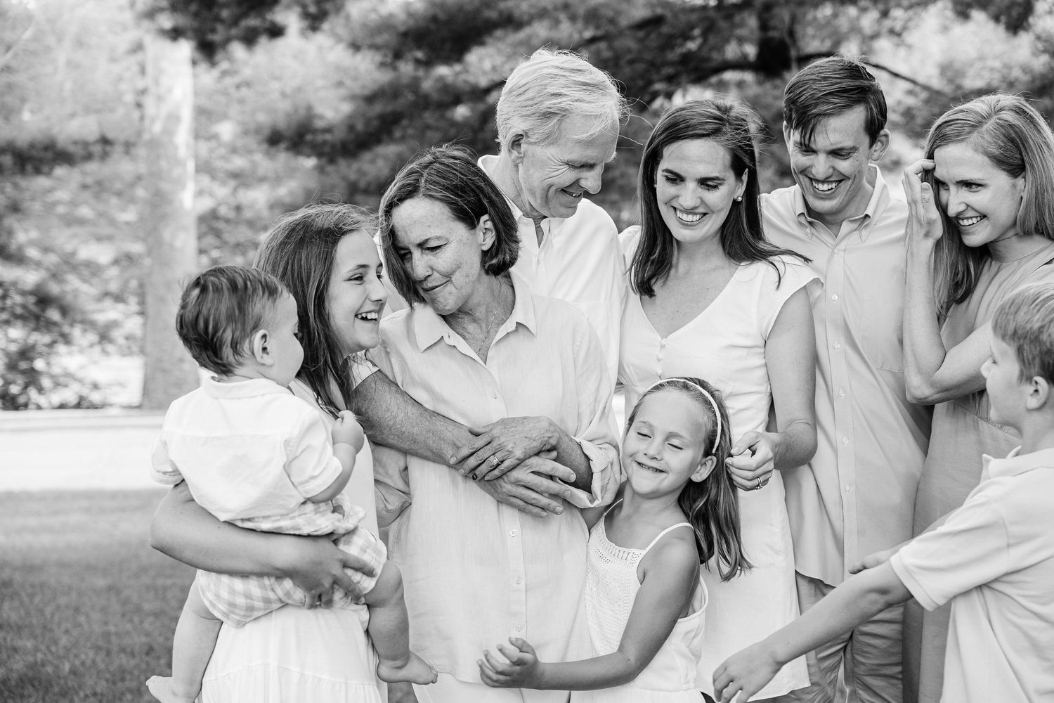 A joyful multi-generational family shares candid moments together outdoors in black and white photography.