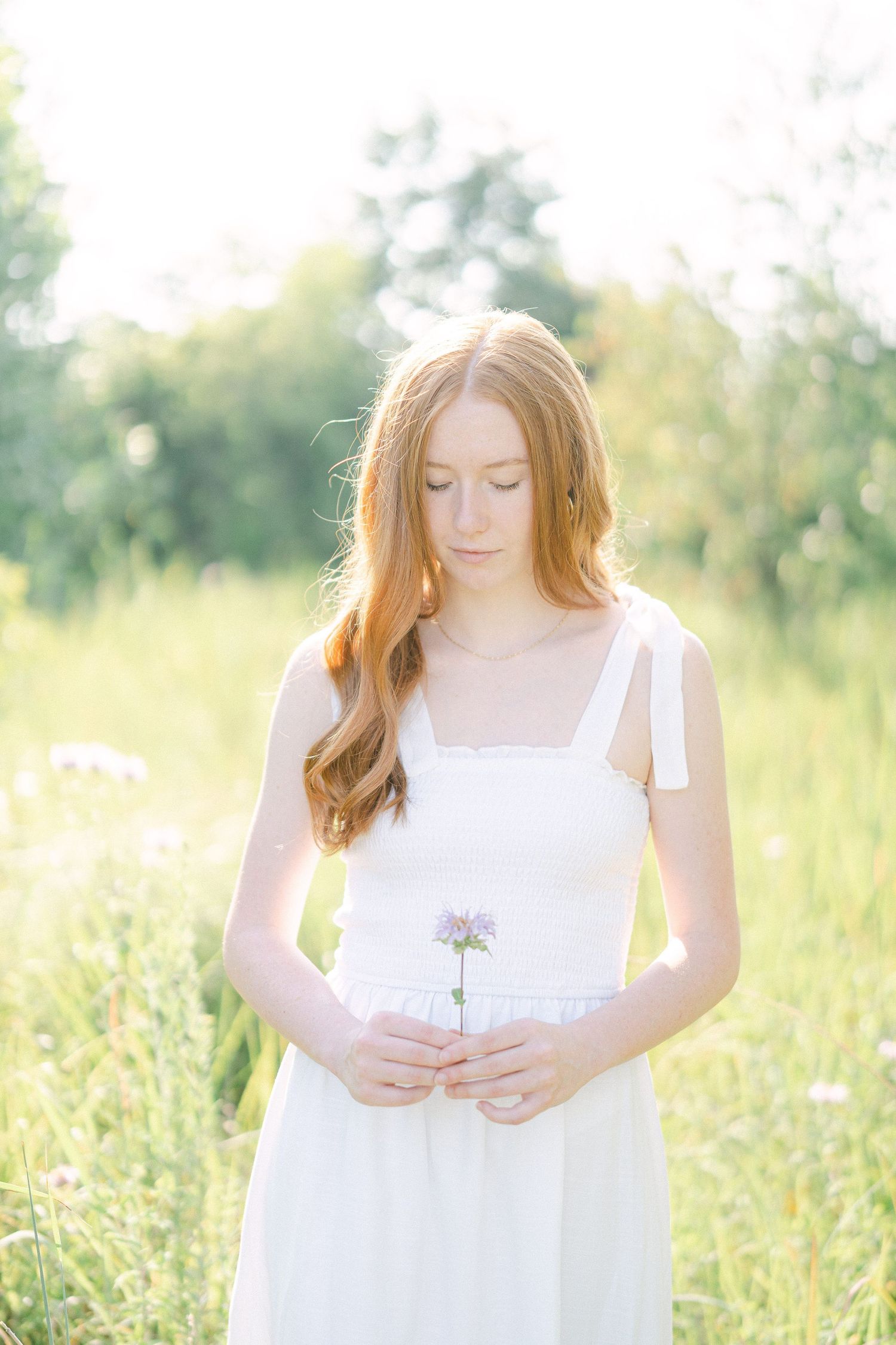 A person in a white sundress stands in a sunlit meadow with wildflowers on a bright summer day.