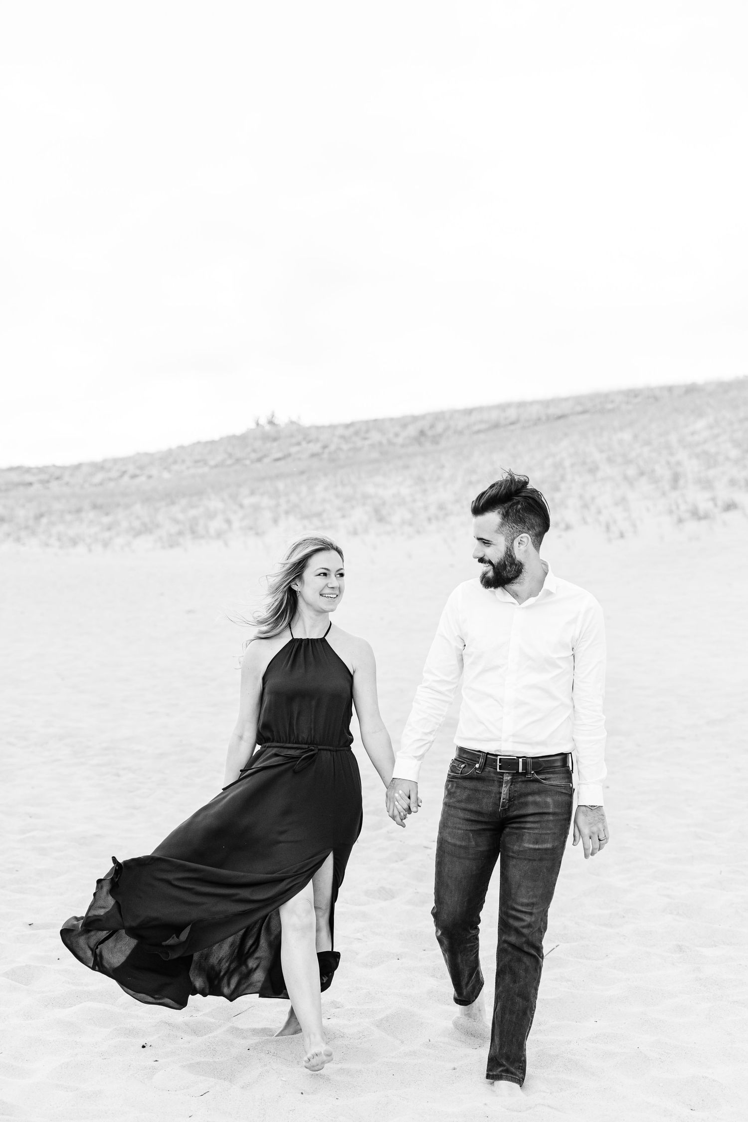 A couple in black and white attire walks together on a sandy beach in a romantic photoshoot sequence.