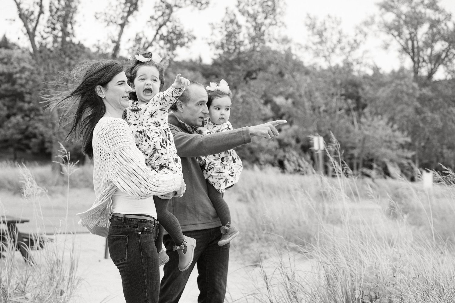 Black and white photo of a joyful group pointing and laughing together in a grassy outdoor field.