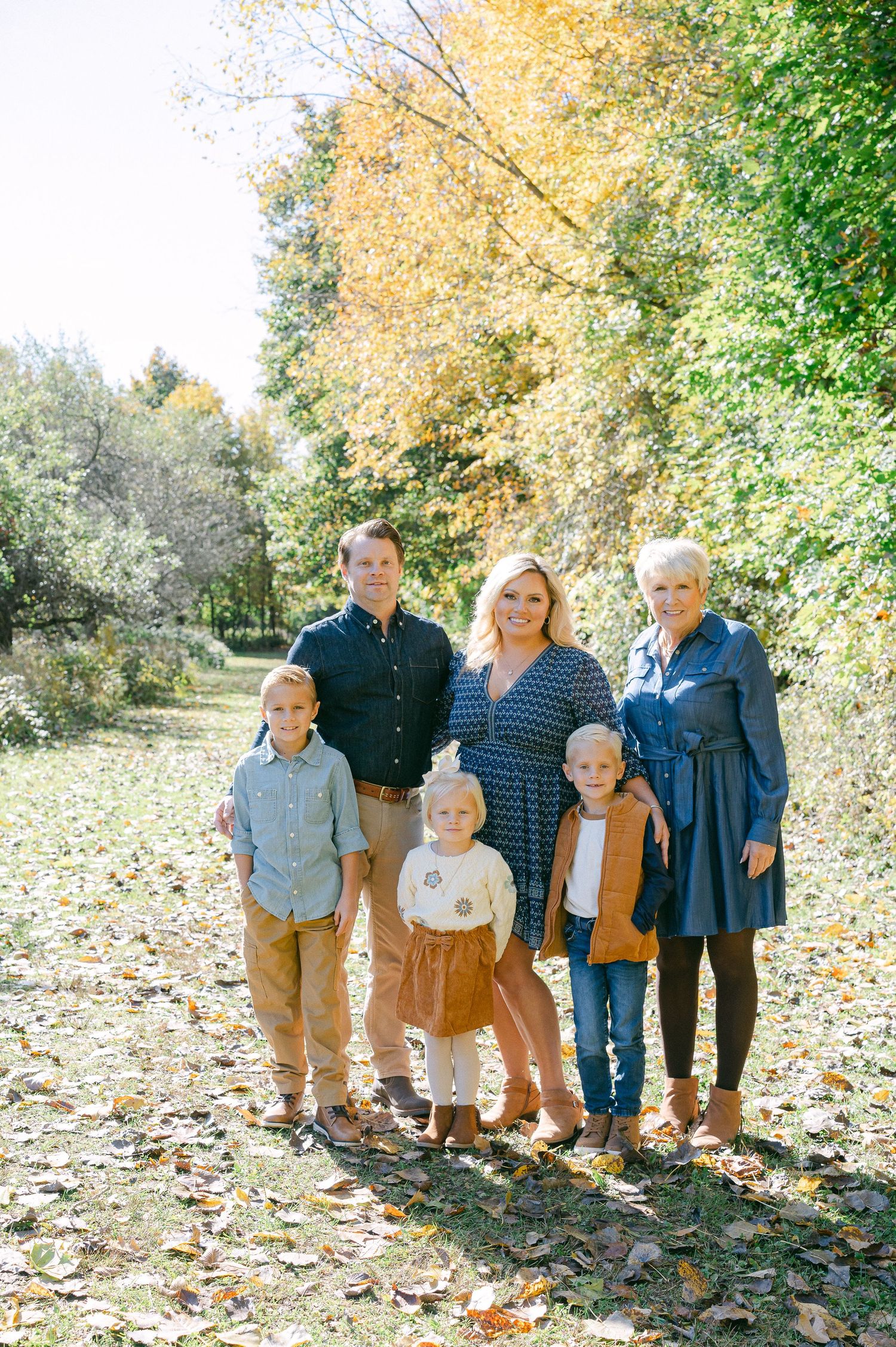 A group stands together on fallen autumn leaves in a park setting with golden foliage in the background.