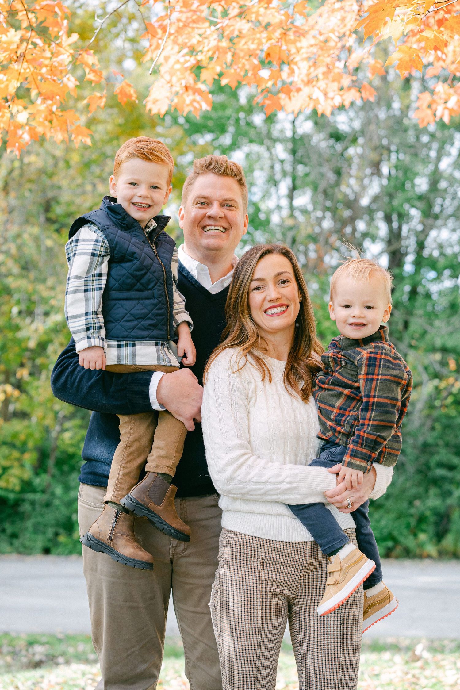 A group poses together outdoors in coordinated fall outfits with autumn foliage in the background.