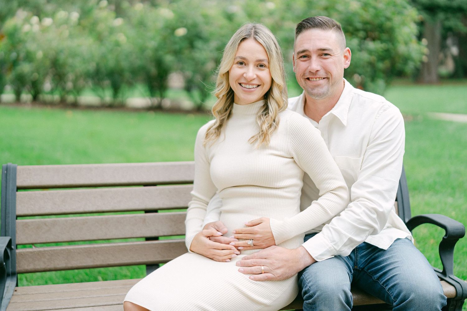 A couple shares romantic moments together on a park bench surrounded by lush greenery on a sunny day.