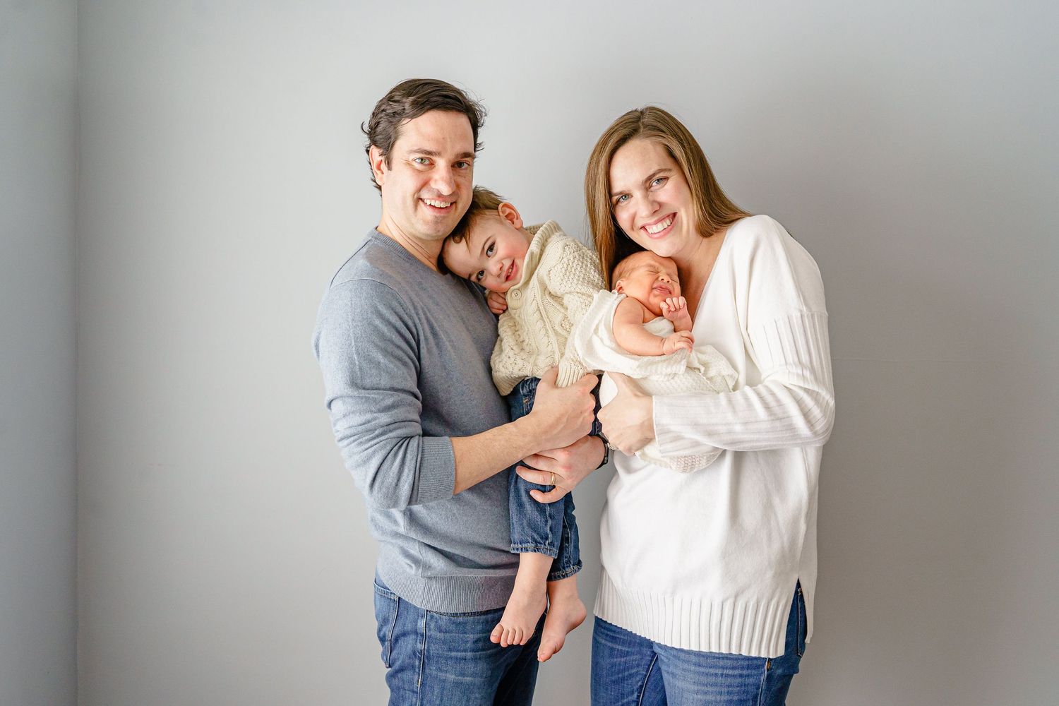 Family in grey and white clothing embracing and sharing intimate moments against neutral background.