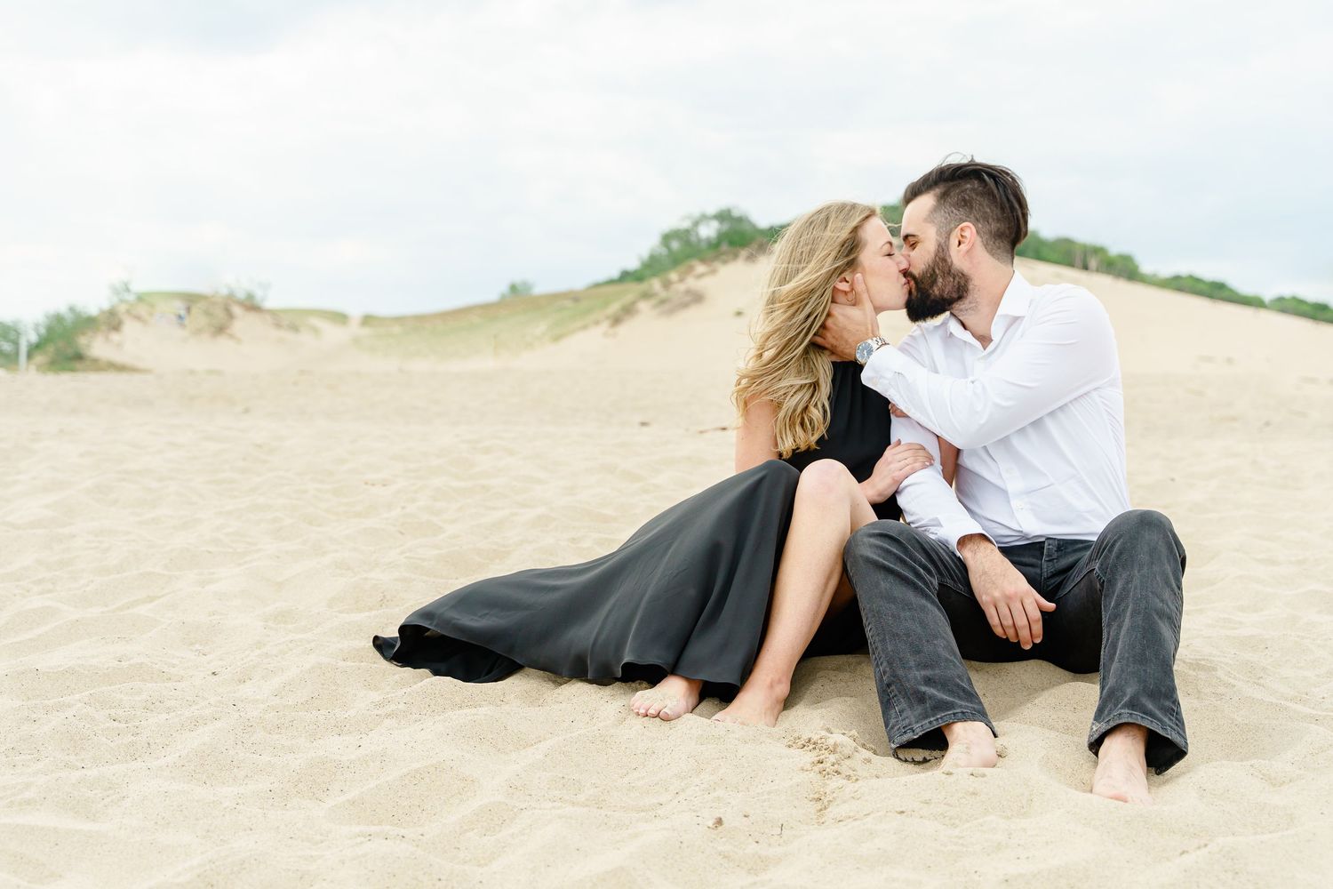 Romantic couple lying together on sandy beach dunes during sunset photoshoot.