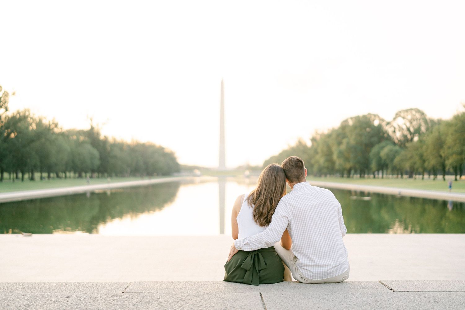 Couple sitting together on a white marble surface overlooking the Washington Monument and National Mall at sunset.