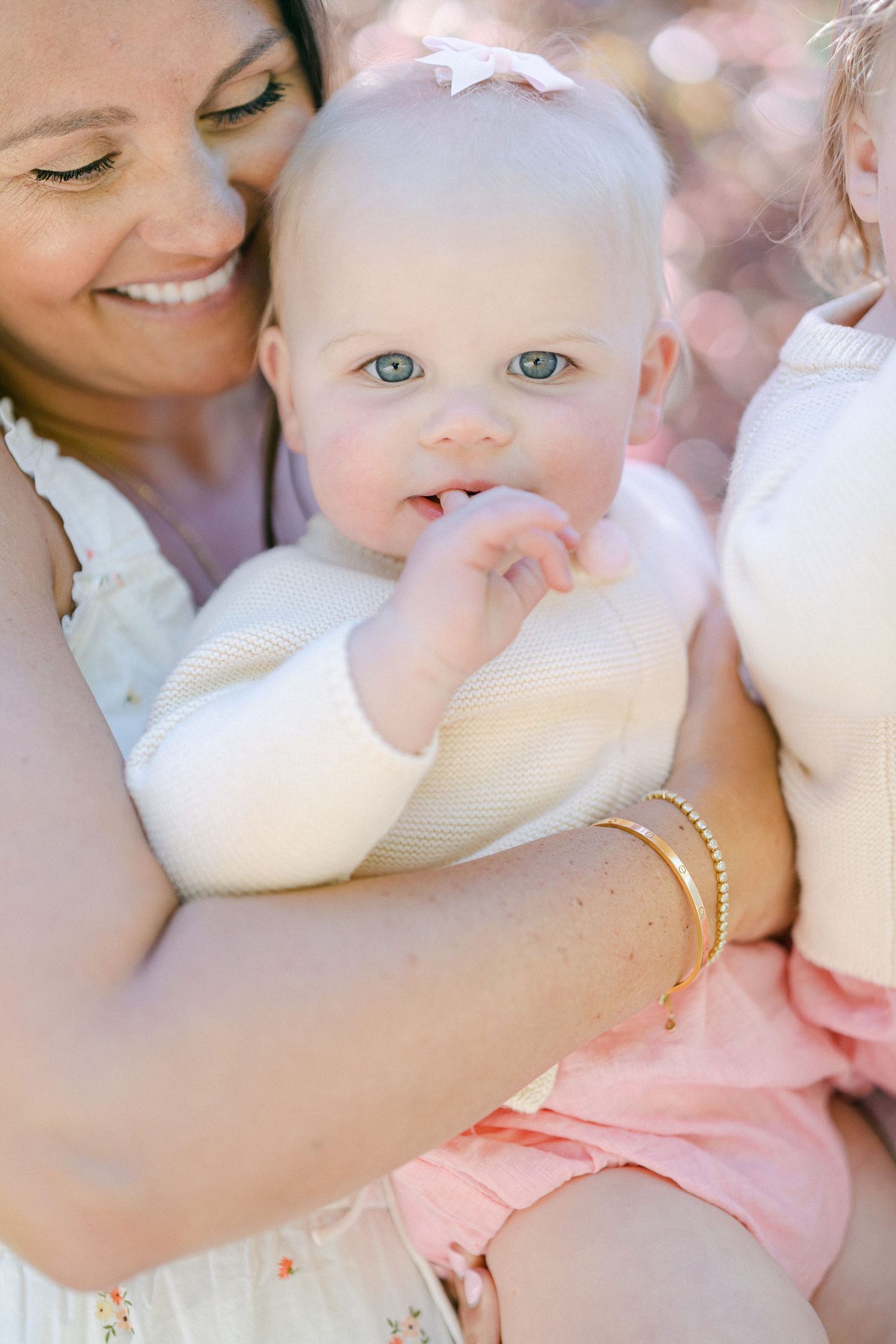 A tender moment captured as a baby in cream sweater and pink bottoms is held lovingly outdoors.