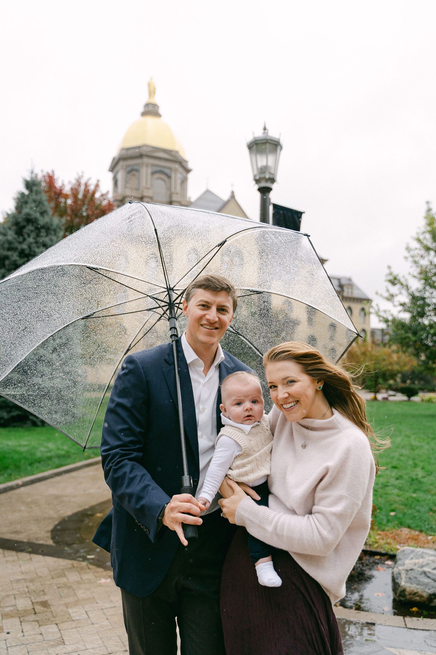 A couple shares tender moments under a clear umbrella on a rainy autumn day near a church building.