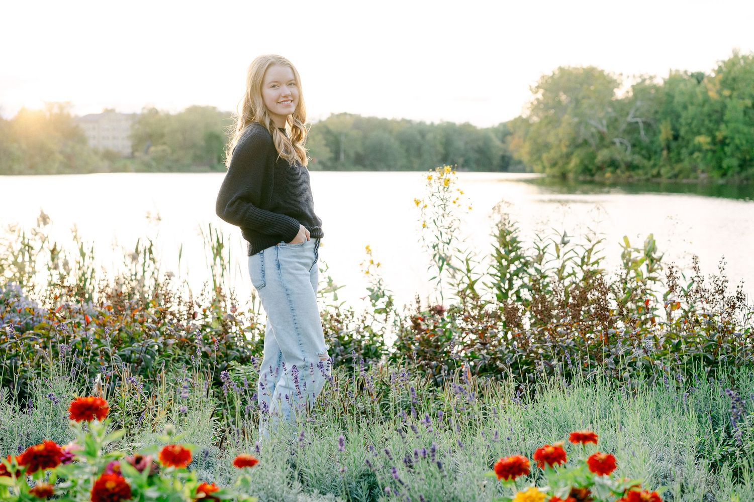 Person in white dress walks through a blooming wildflower meadow with red poppies and white flowers at sunset.