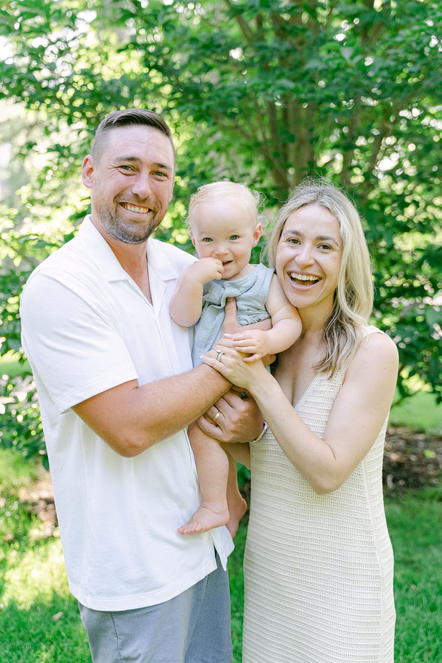 Family shares joyful moments together outdoors in coordinated white and beige outfits on a sunny summer day.