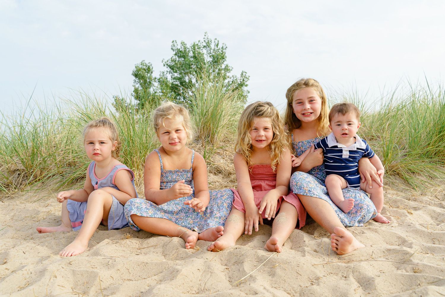 Children's feet lined up in a row on sandy beach dunes during summer vacation photo session.