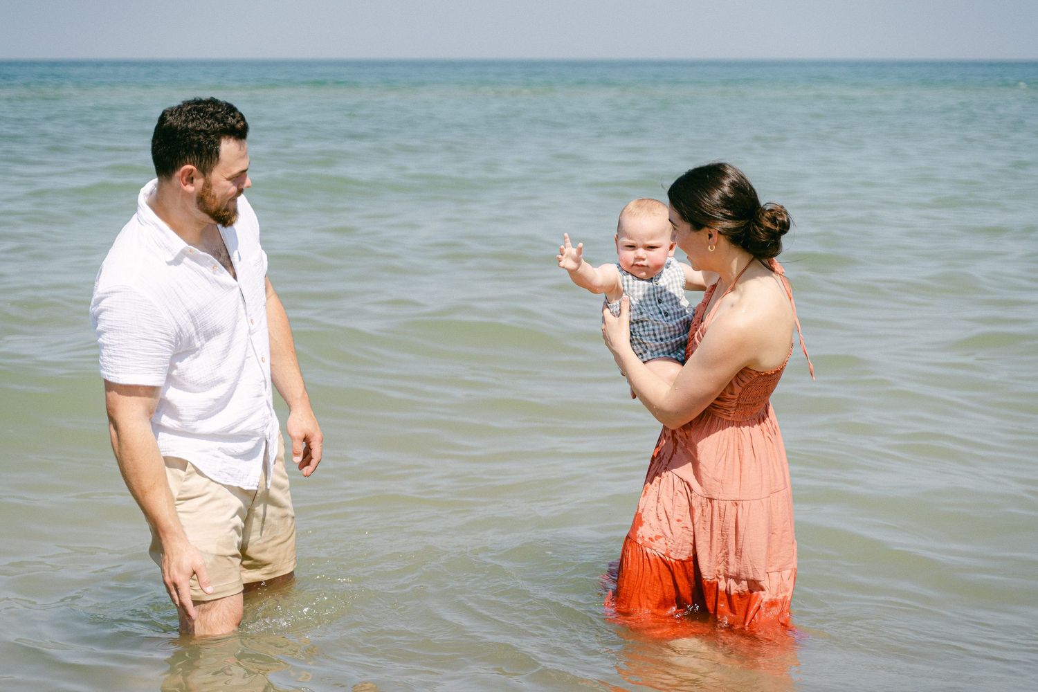 Family enjoying a sunny day playing and splashing together in shallow ocean waters at the beach.