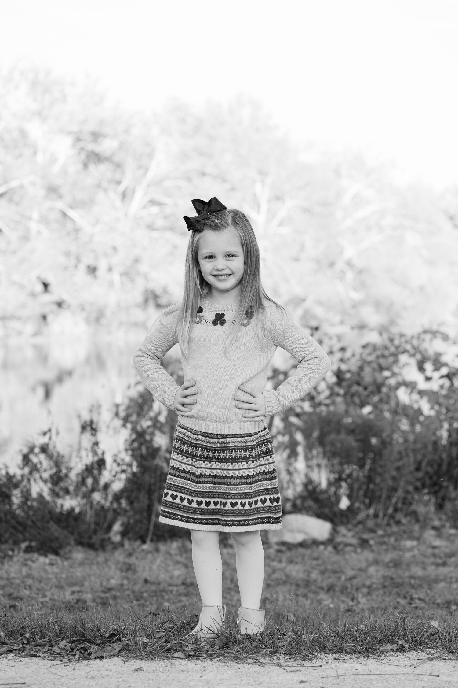 A young child in a patterned dress stands on grass while striking playful poses in black and white.