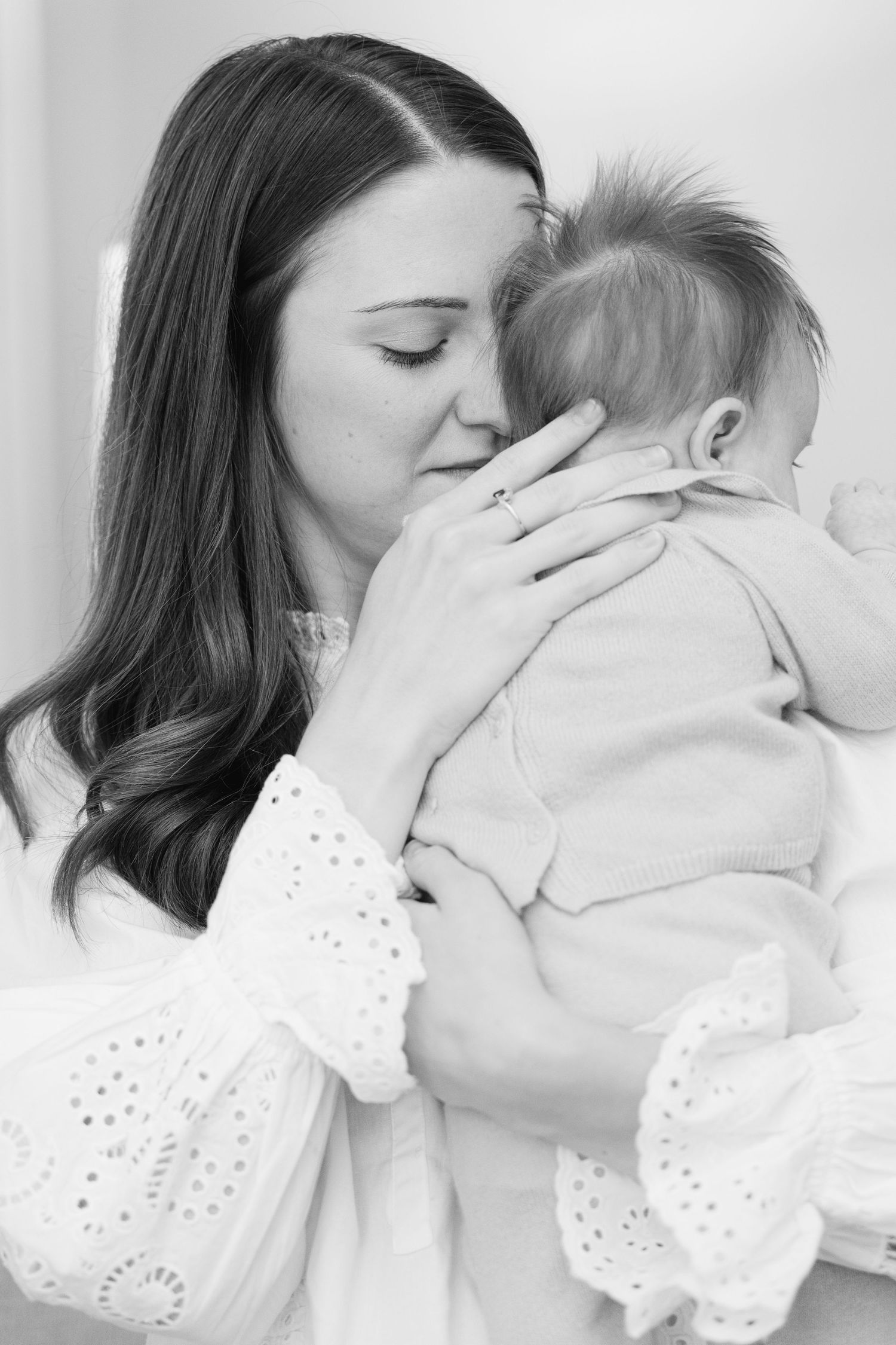 A tender black and white photo series showing a mother in white eyelet dress embracing and kissing her baby.