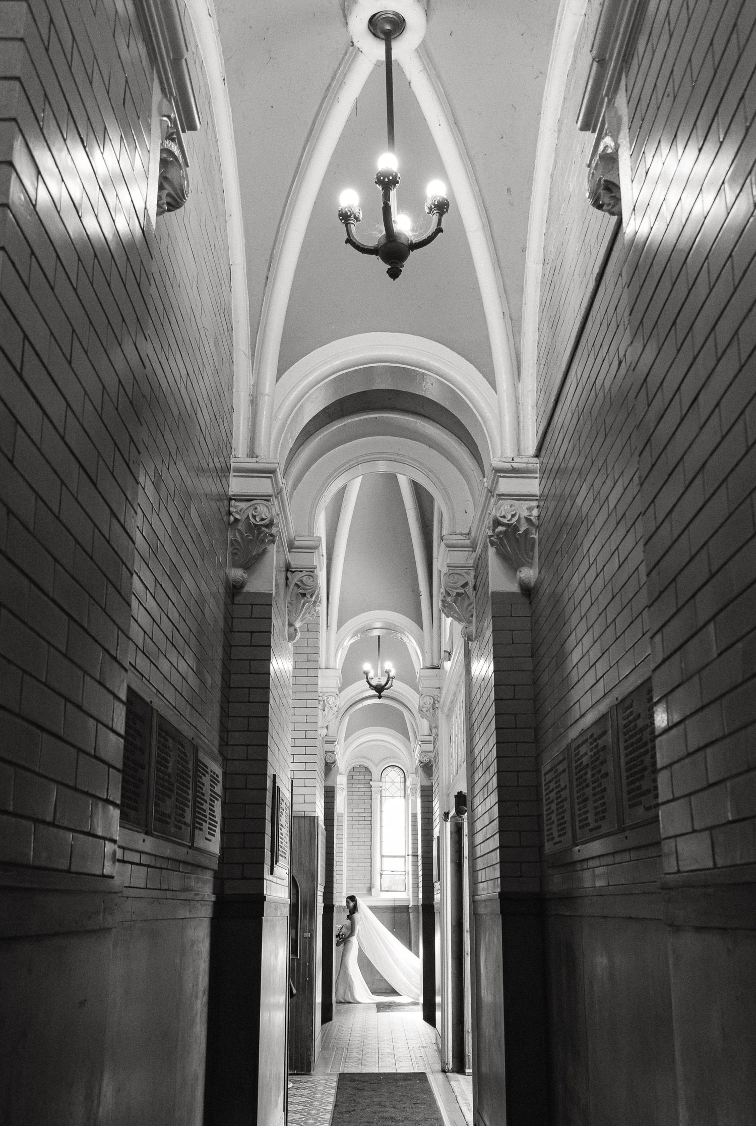 Black and white photo of an elegant arched hallway with chandelier lighting and a lone figure standing in the distance in Chicago, IL
