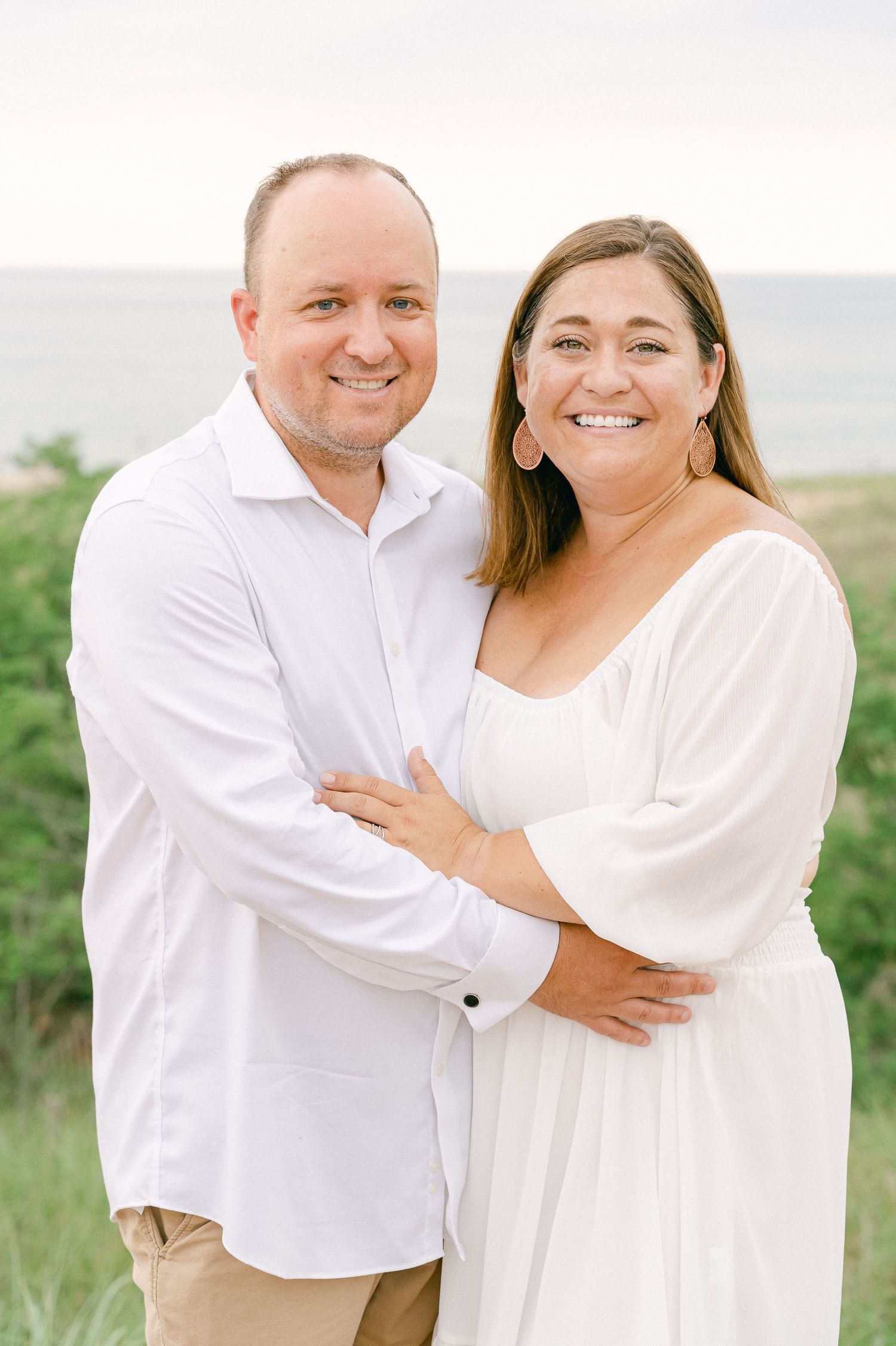 Romantic beach photo session with couple wearing white outfits against coastal backdrop.