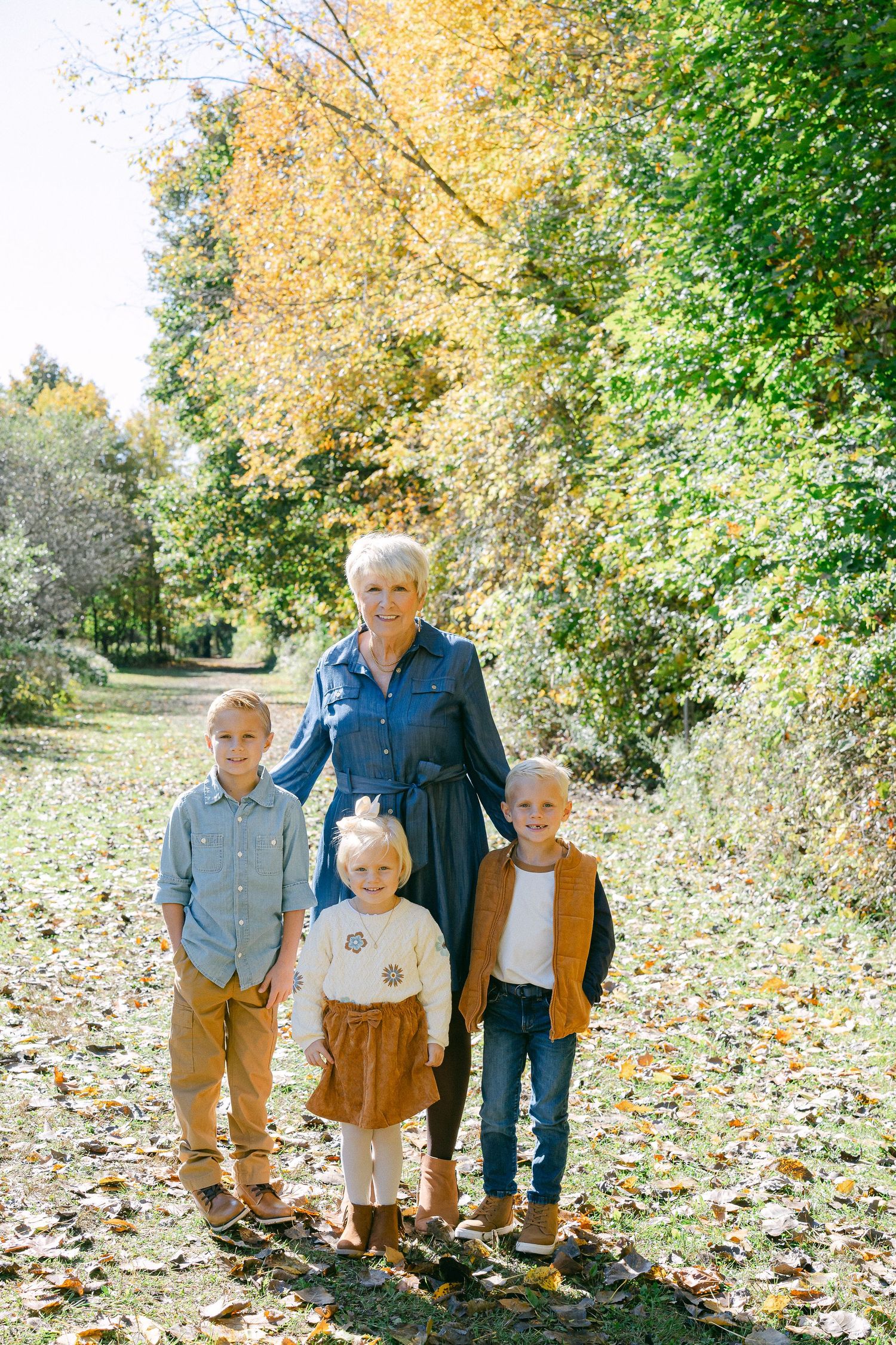 A family walks together on a leaf-covered autumn trail in the woods surrounded by golden foliage.
