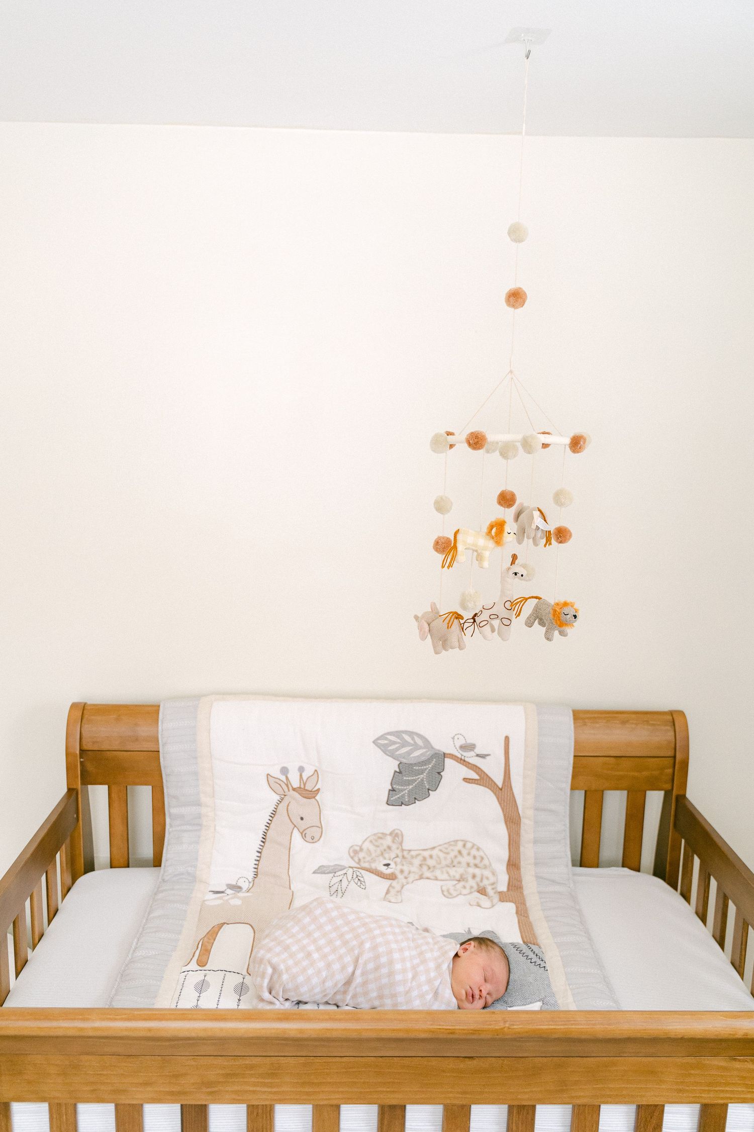 A wooden baby crib with white bedding and animal-themed artwork displayed on the wall above it.