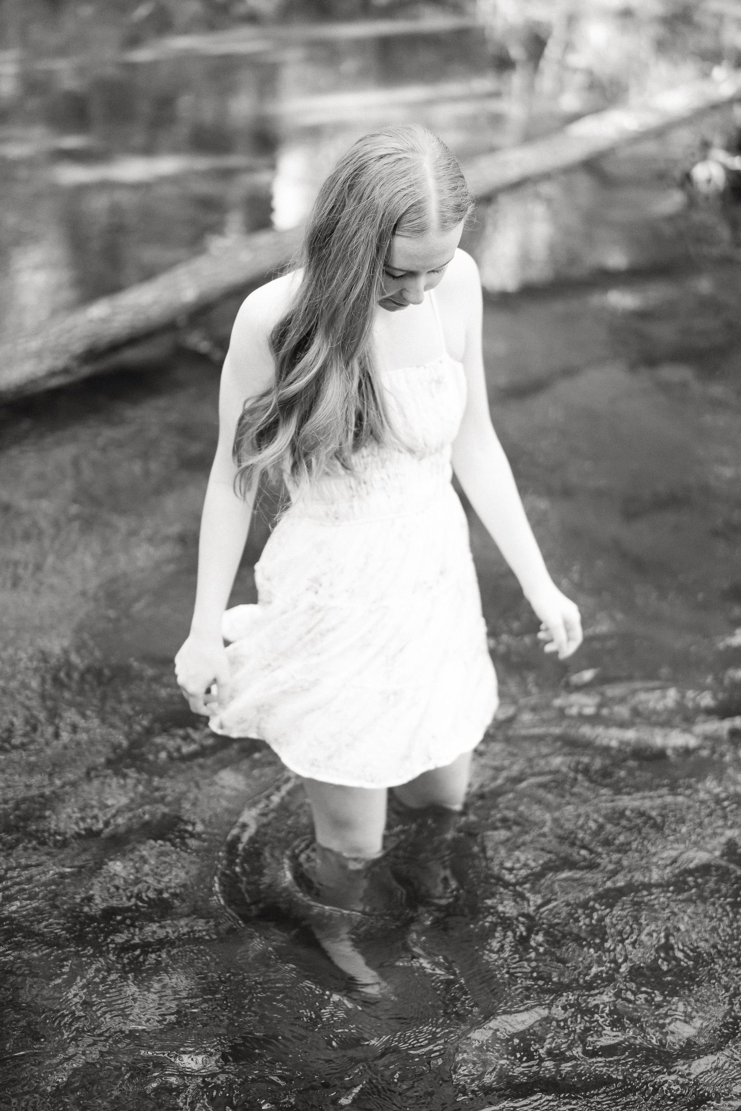A dreamy black and white portrait of someone in a white dress wading through shallow water.