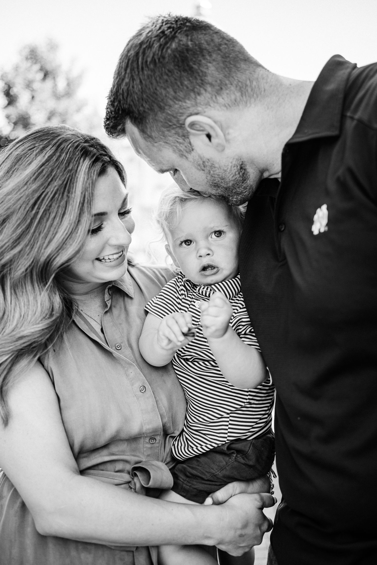 A candid black and white photo series showing playful family moments with a toddler in a striped shirt.