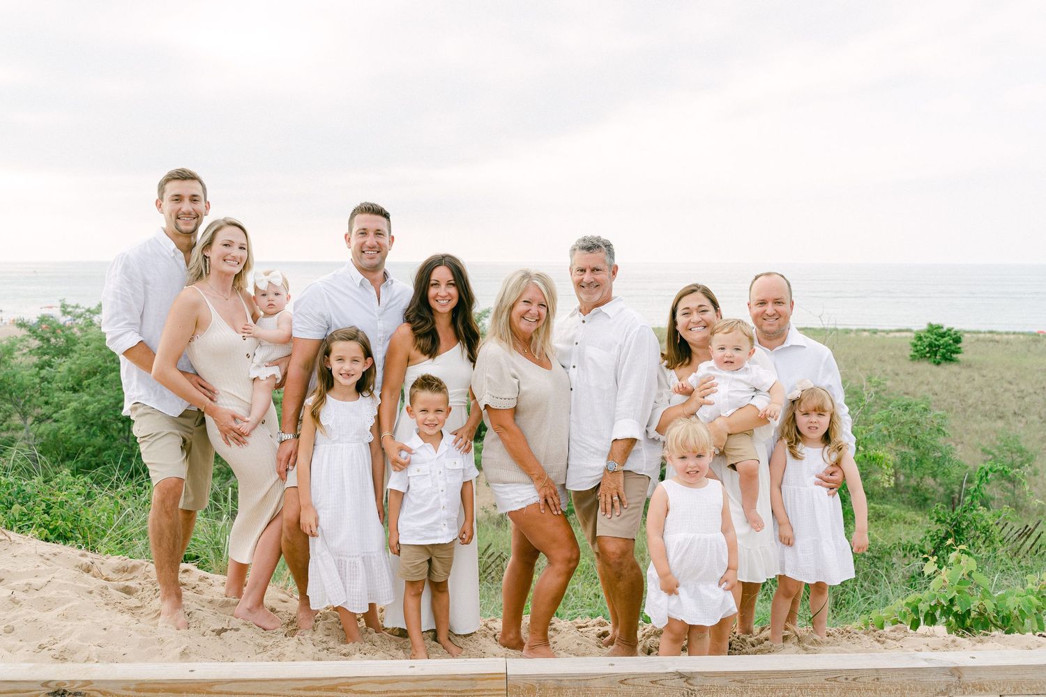 A group wearing coordinated white and tan outfits poses together on a grassy hillside by the ocean.