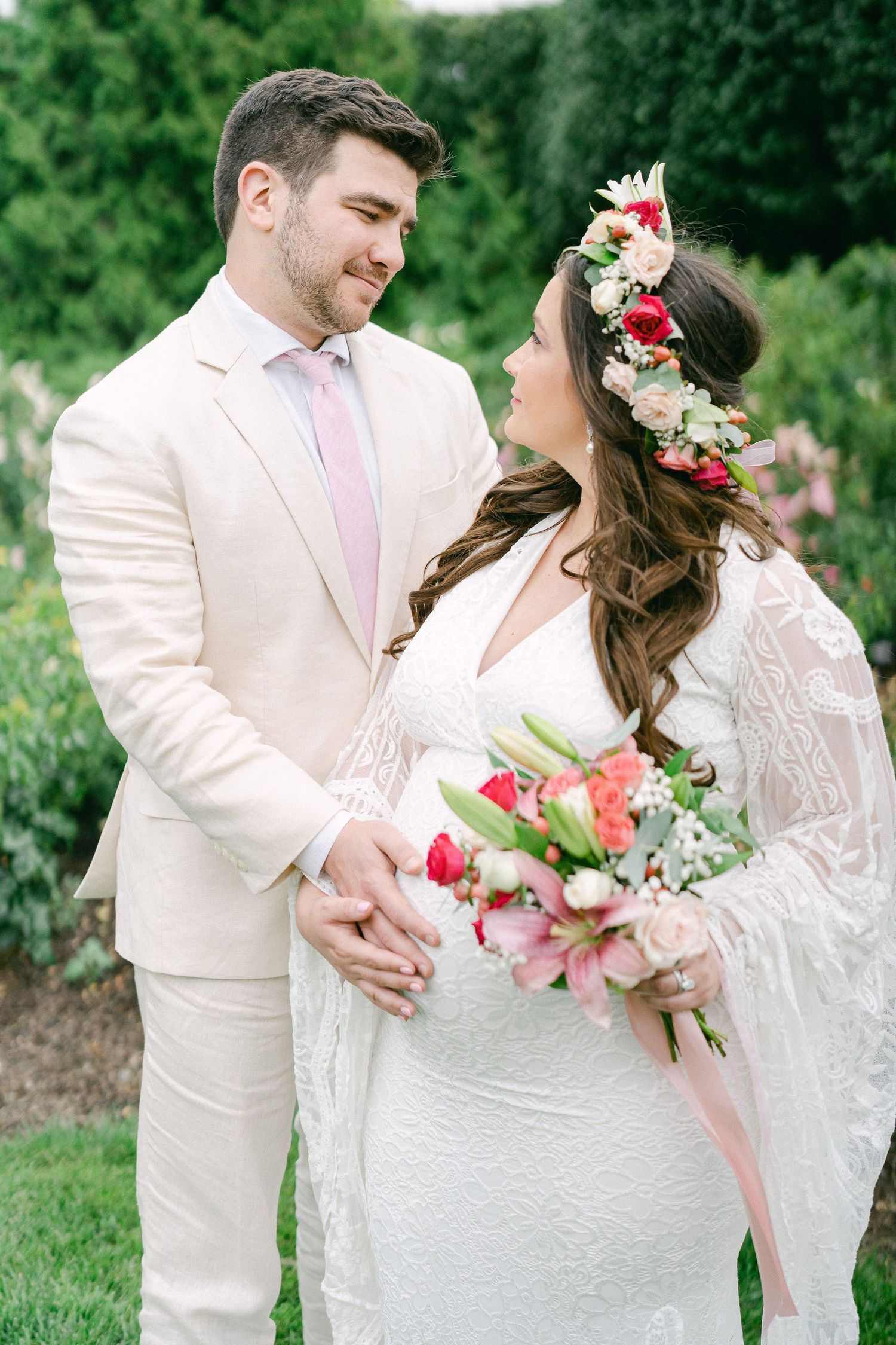 Romantic outdoor wedding portraits showcase a couple in cream and white attire with pink floral accents in a garden setting.