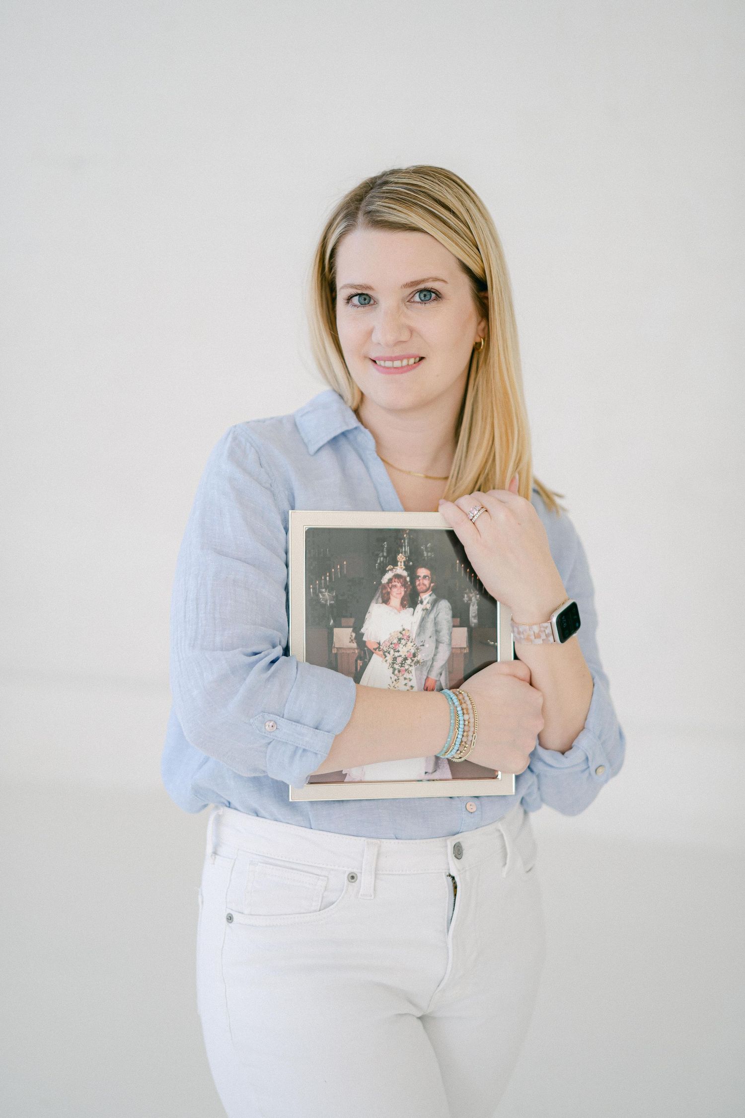A person in a light blue shirt and white pants holds a photo album against a white background.
