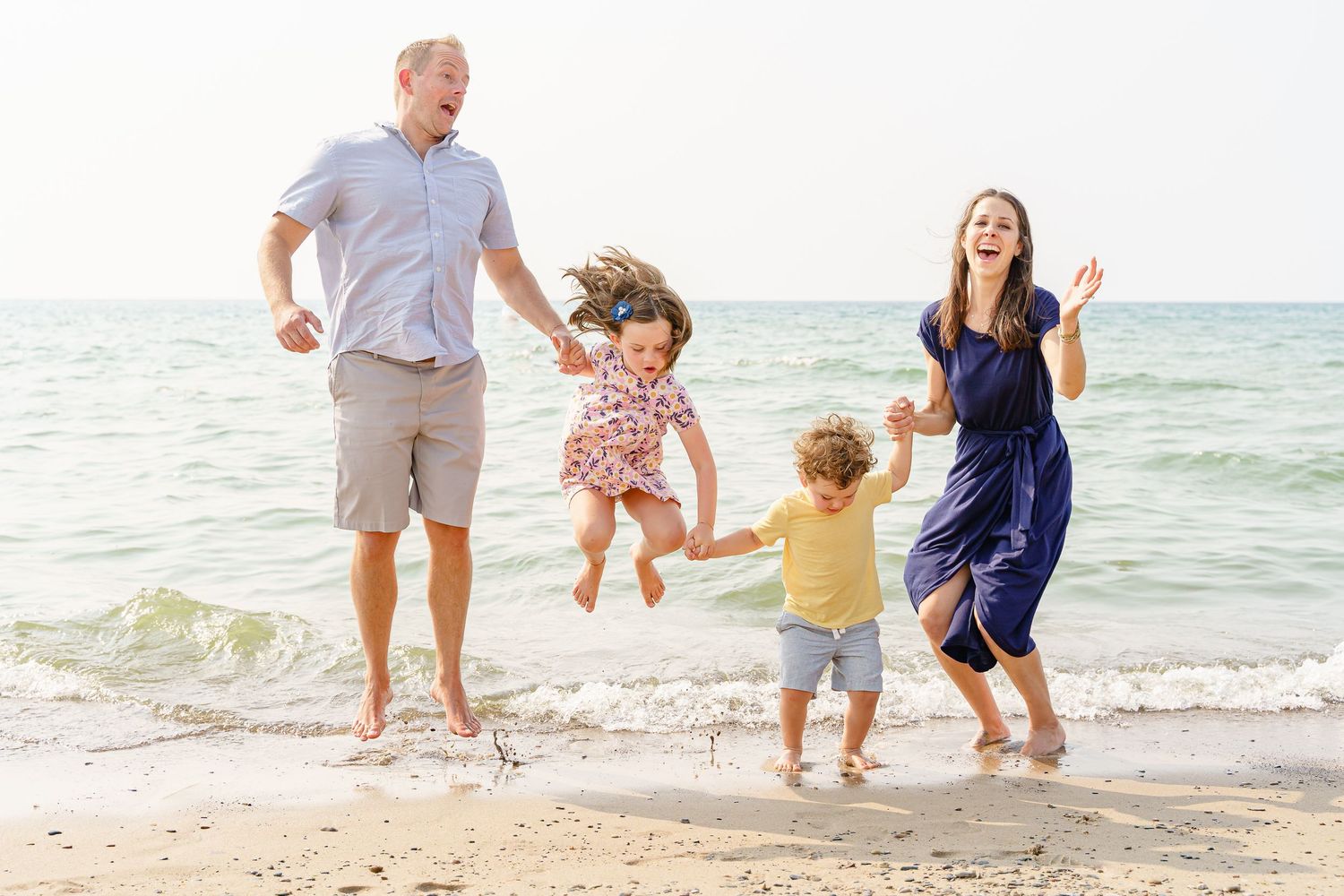 Family playing and running together along a sunny beach with ocean waves in the background.