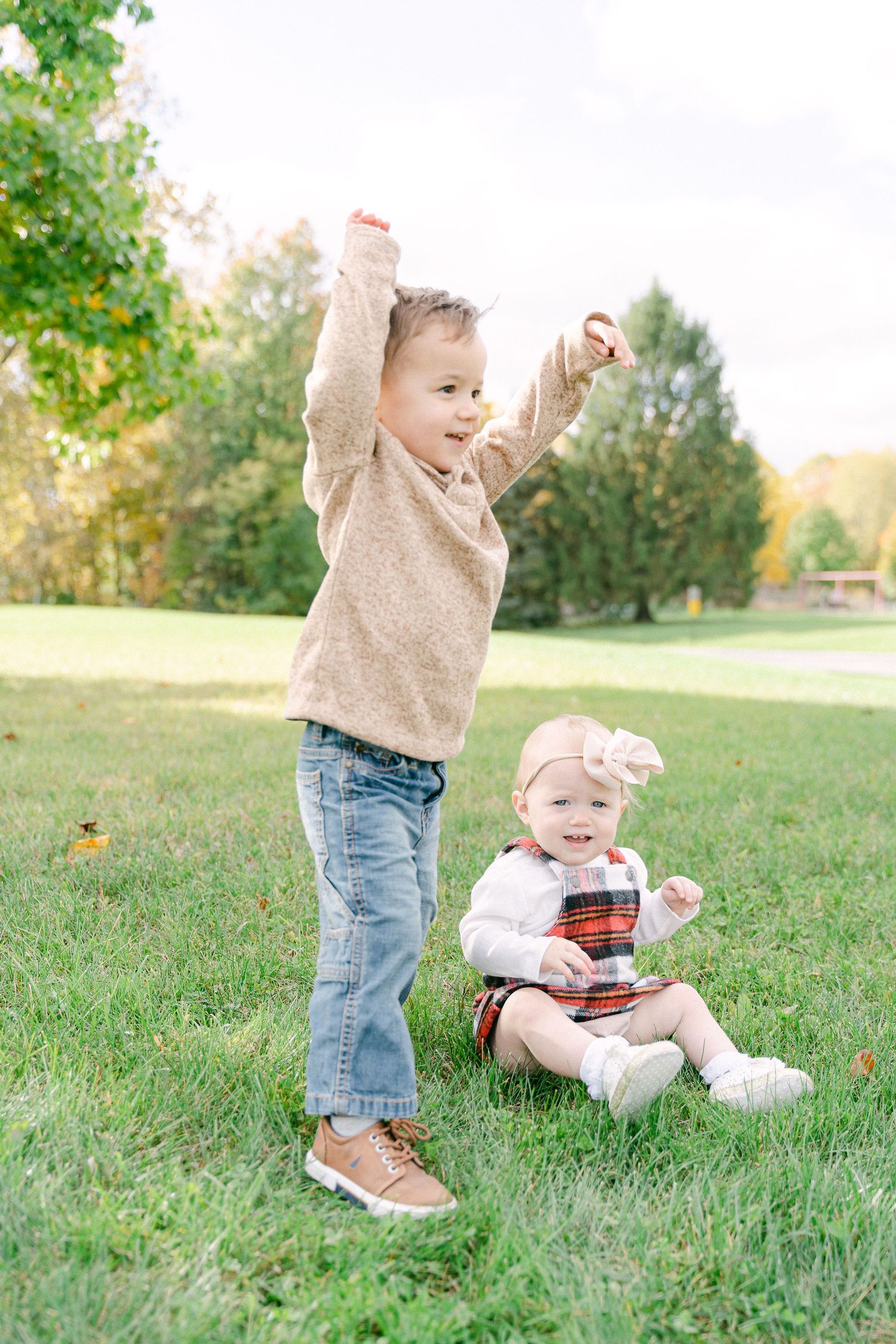 Two small children play together on grassy lawn during golden hour in autumn.