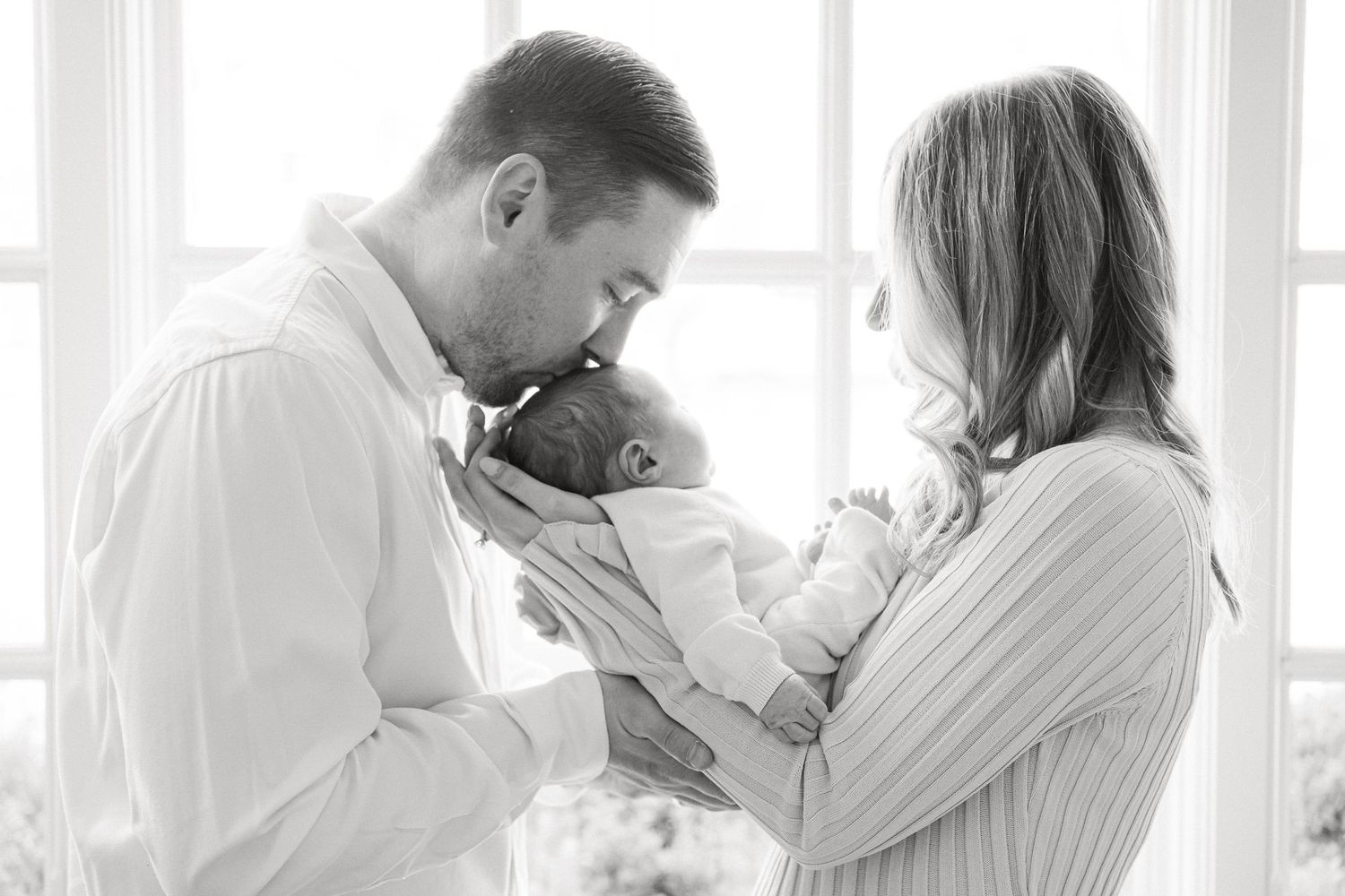 A couple in white outfits share tender moments together in a bright, minimalist setting.