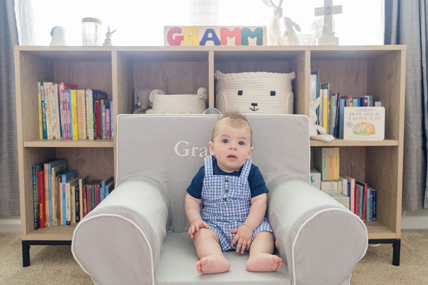 A cozy nursery room with white furniture, bookshelves, and soft gray decor.