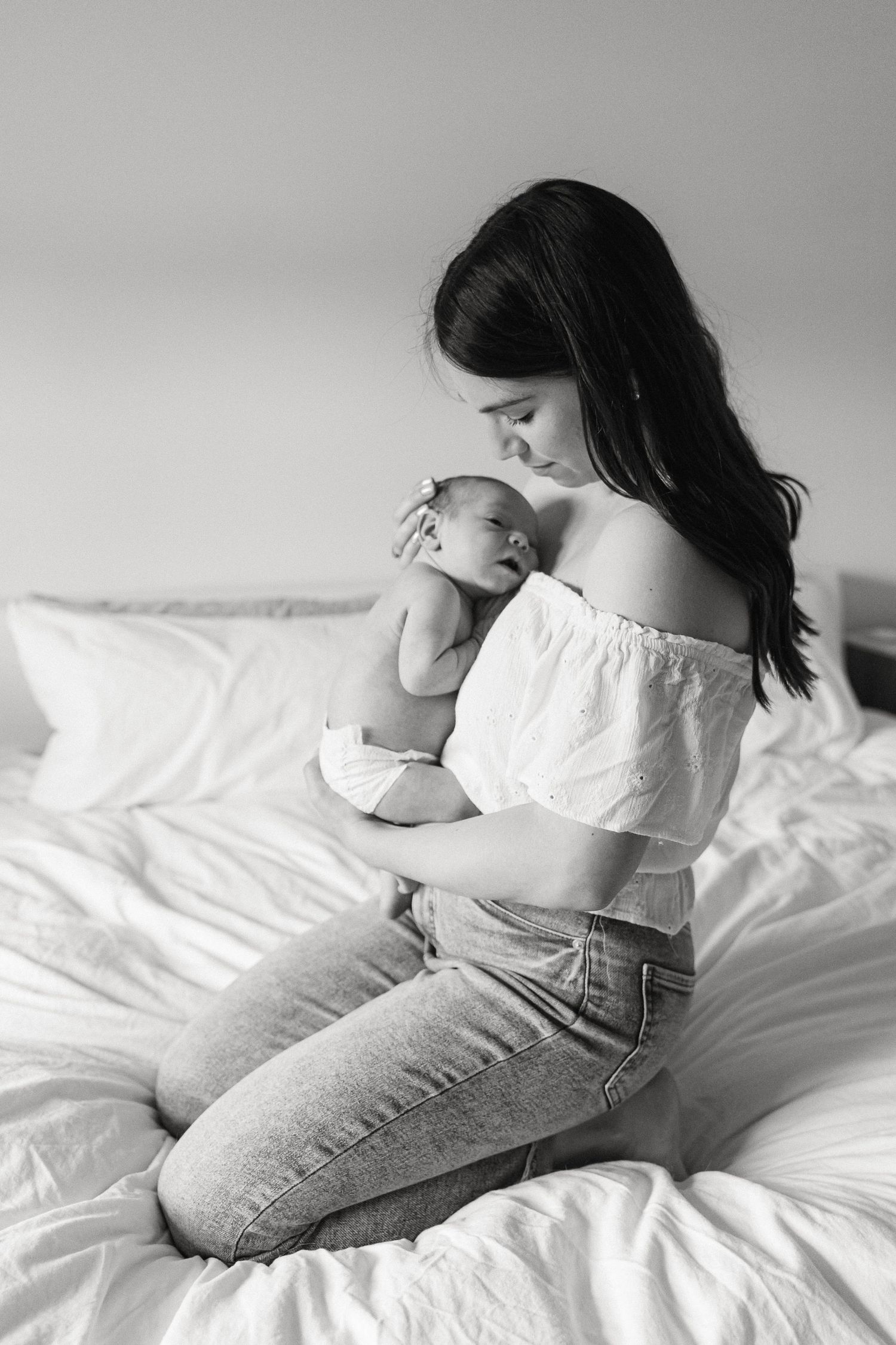 Black and white photo of mother and newborn sharing an intimate moment on white bedding.