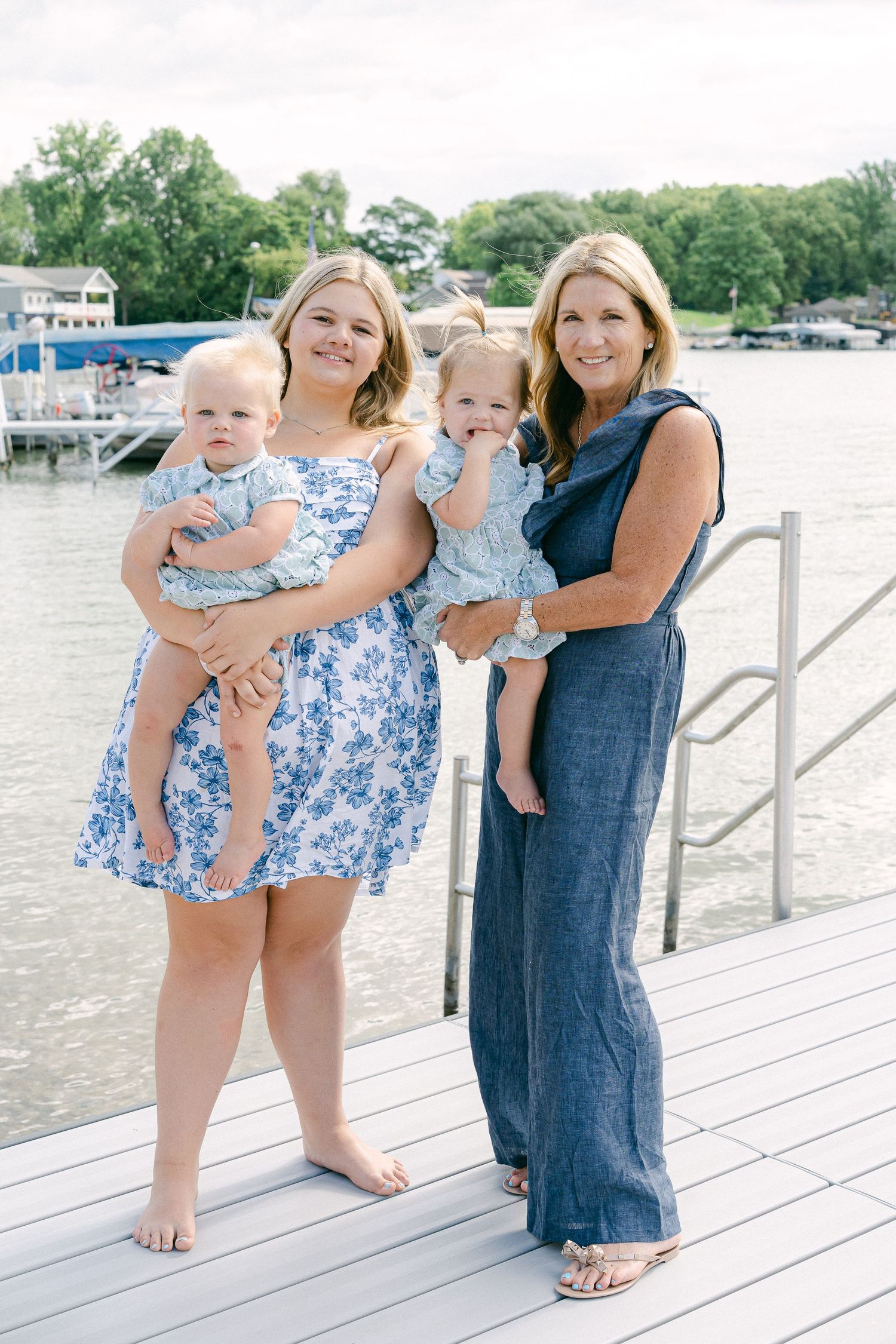 People in blue and floral outfits share joyful moments together on a wooden dock by the water on a sunny day.
