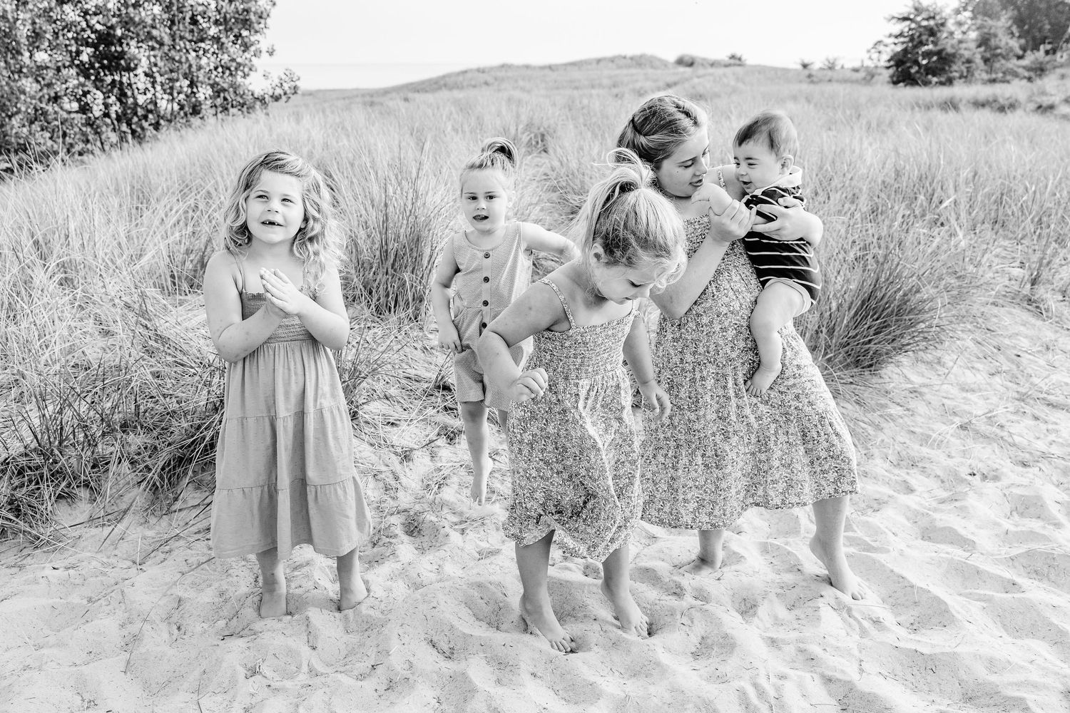 A group of children play and laugh together while walking along a grassy outdoor path in black and white.