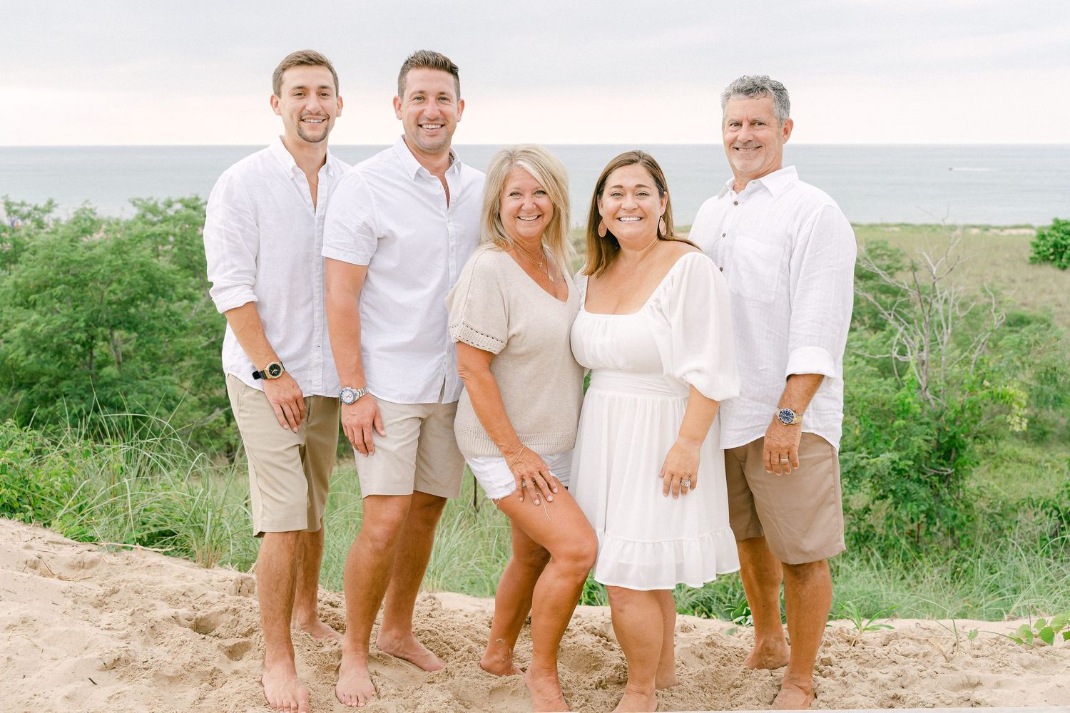 A group wearing coordinated white and beige outfits poses together outdoors for a casual family photoshoot.