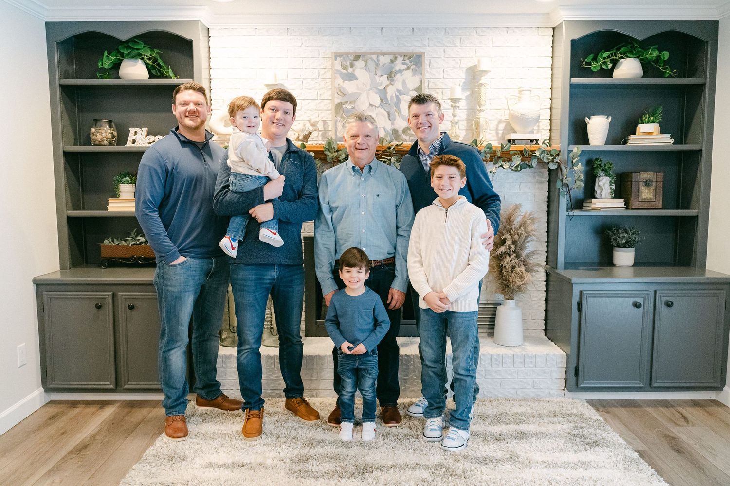 A group of people wearing blue and gray casual attire pose together in a modern living room setting.